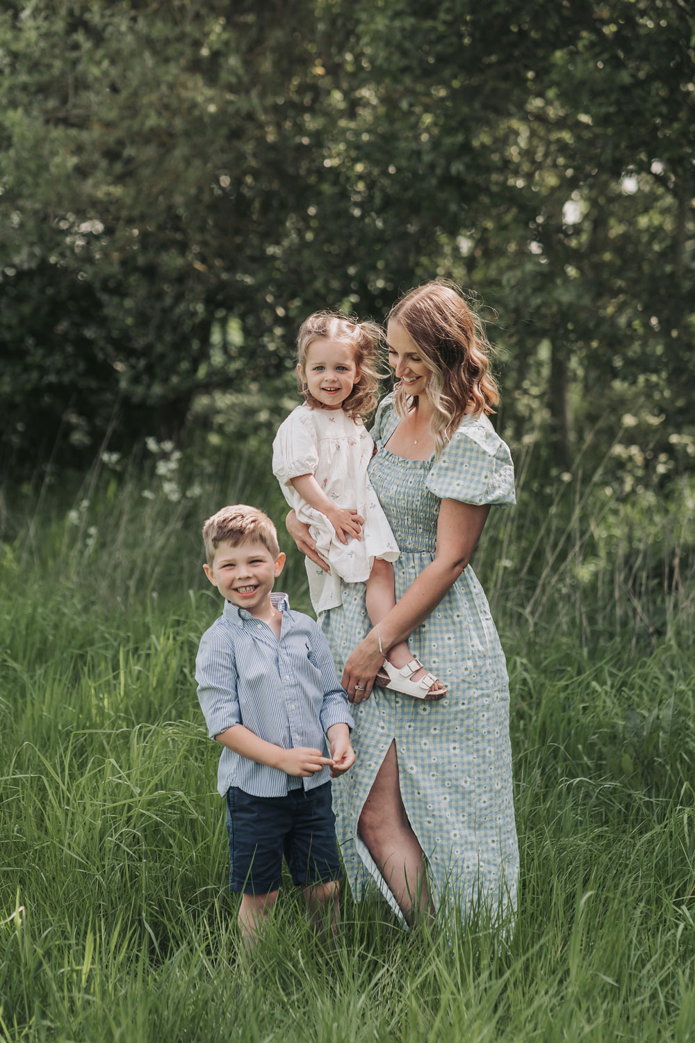 Mum holding daughter and son standing next to her smiling at outdoor Warwickshire family photoshoot