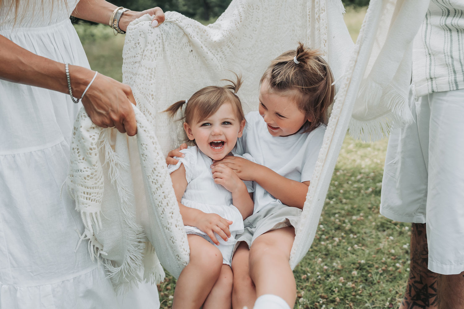 Two children giggling being swung in blanket at outdoor family photoshoot by The Corbett Creative Photography