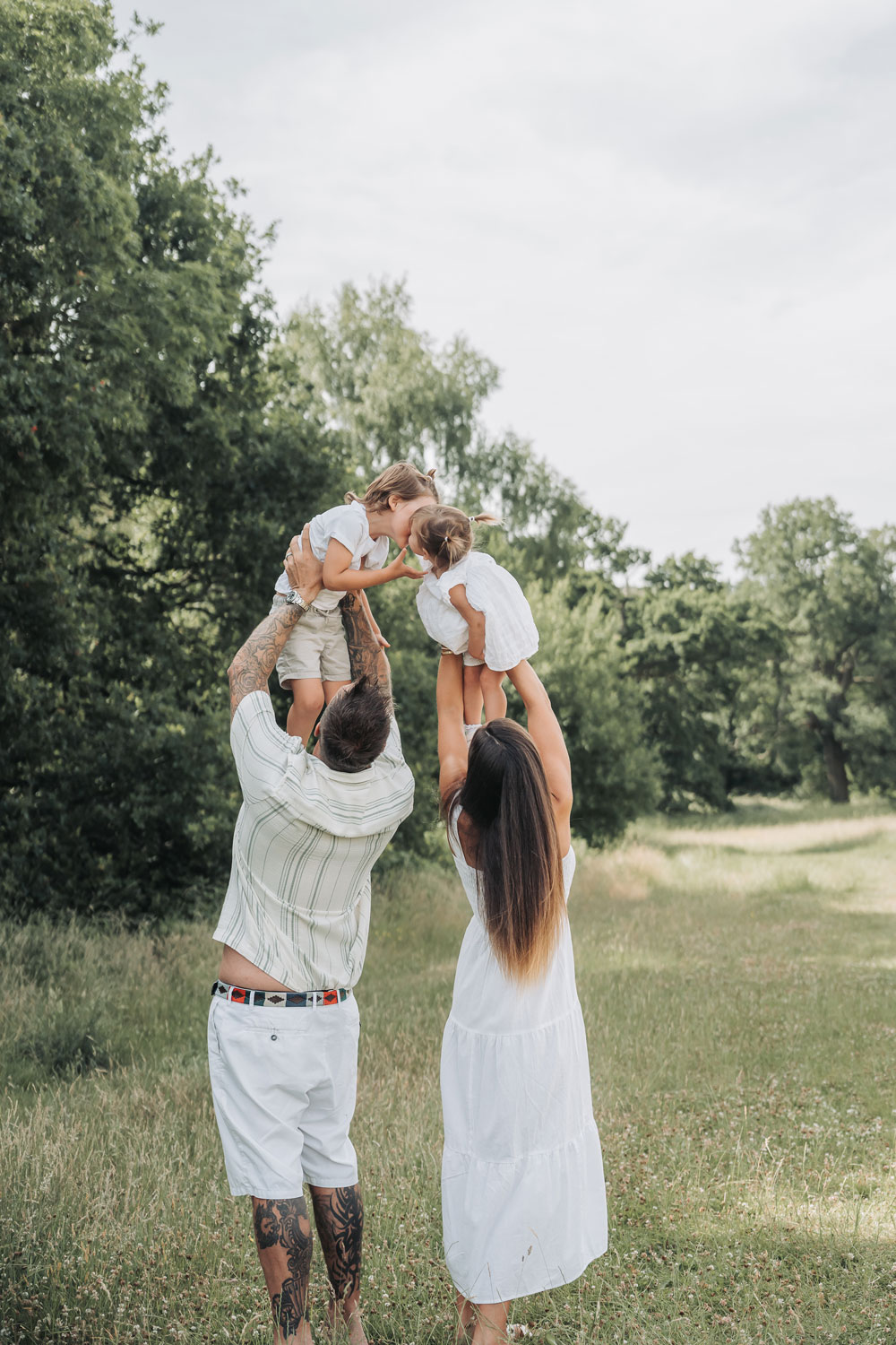 The back of two parents lifting their children up to kiss at a Warwickshire field at a family photoshoot
