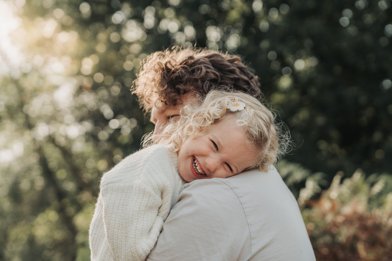 Blonde curly haired girl resting on dad's shoulder smiling at camera by The Corbett Creative Photography