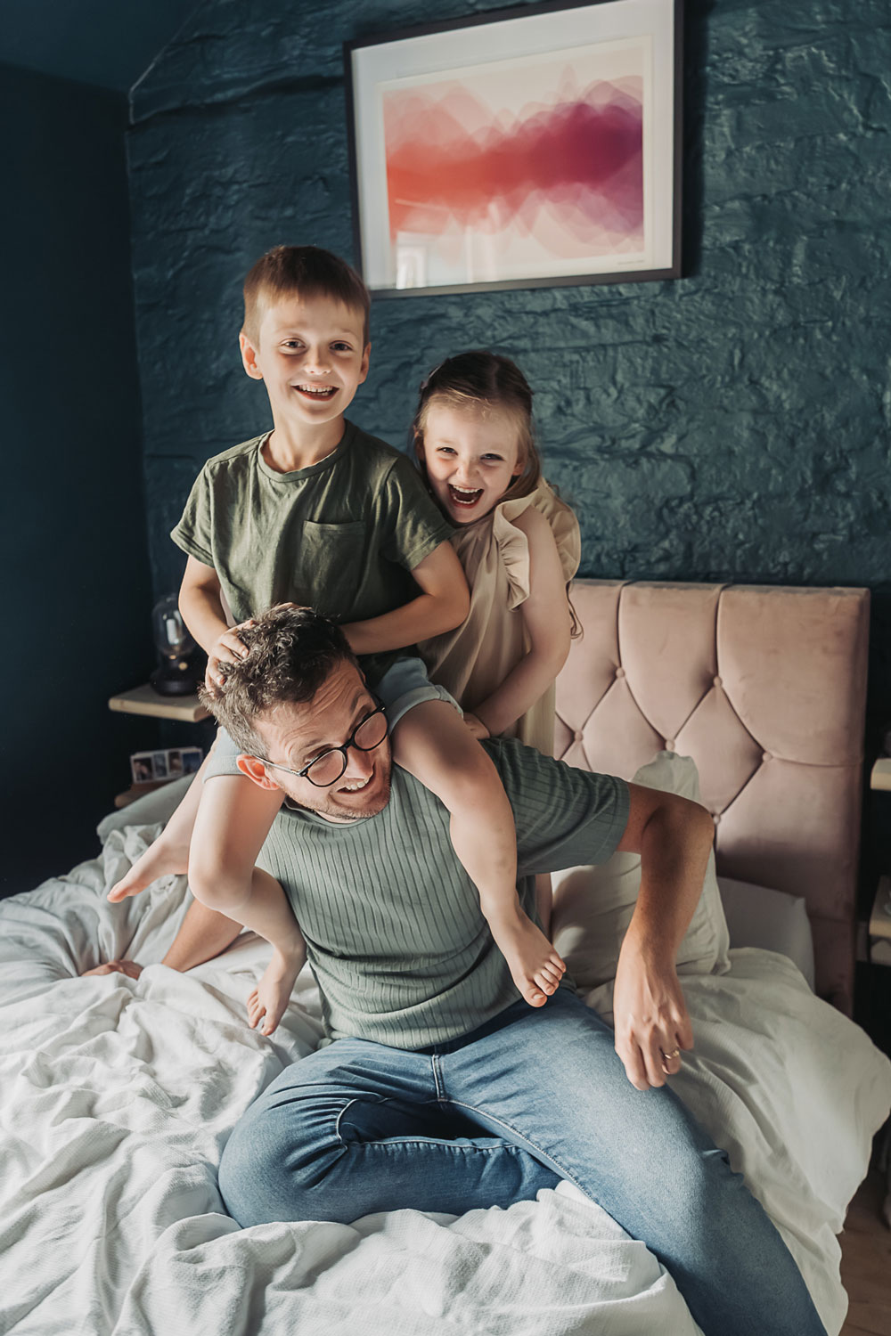 two kids on dads shoulders on bed during an at home photoshoot by the corbett creative photography