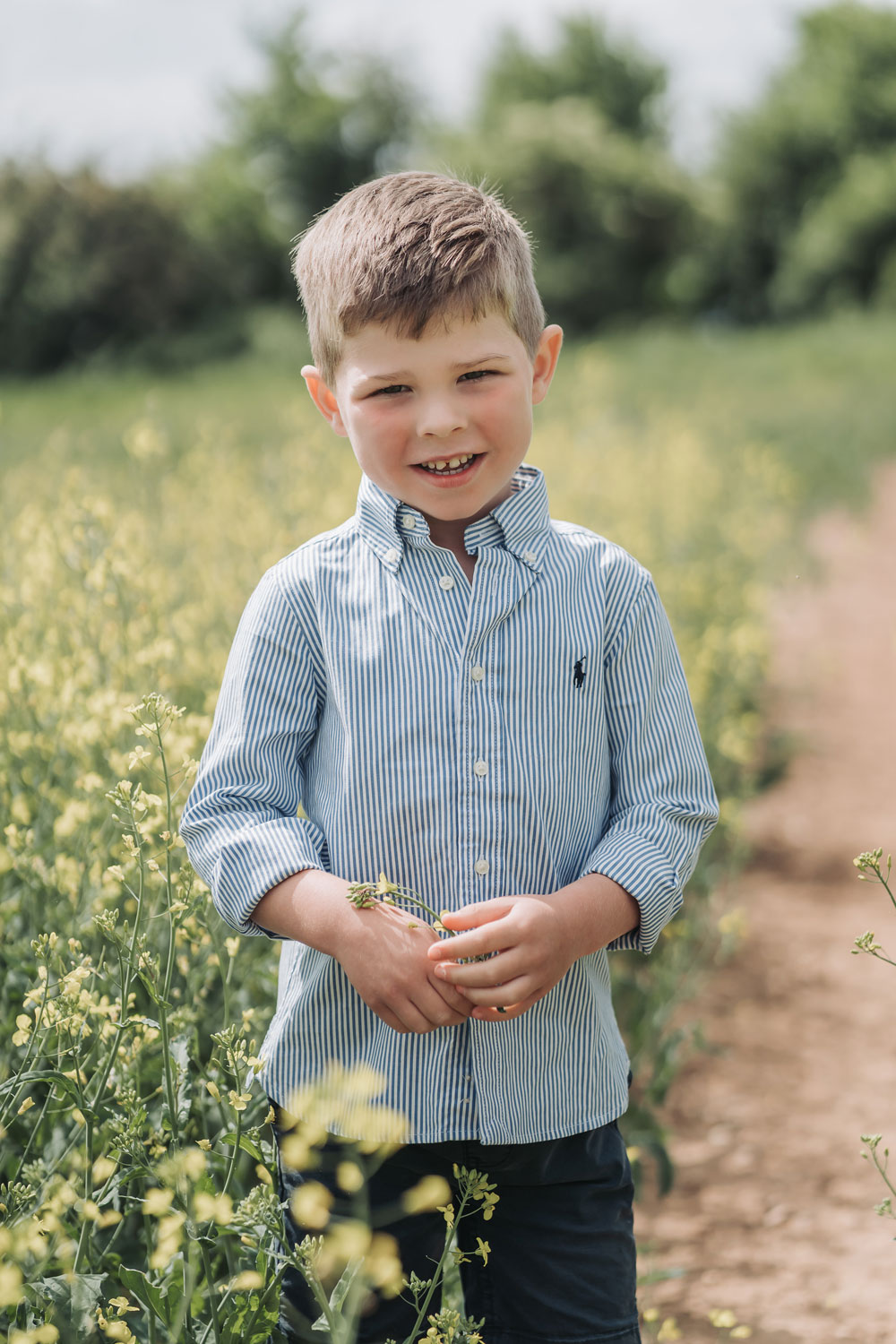 boy holding yellow flower in crop field at Wootton Park at a family photoshoot