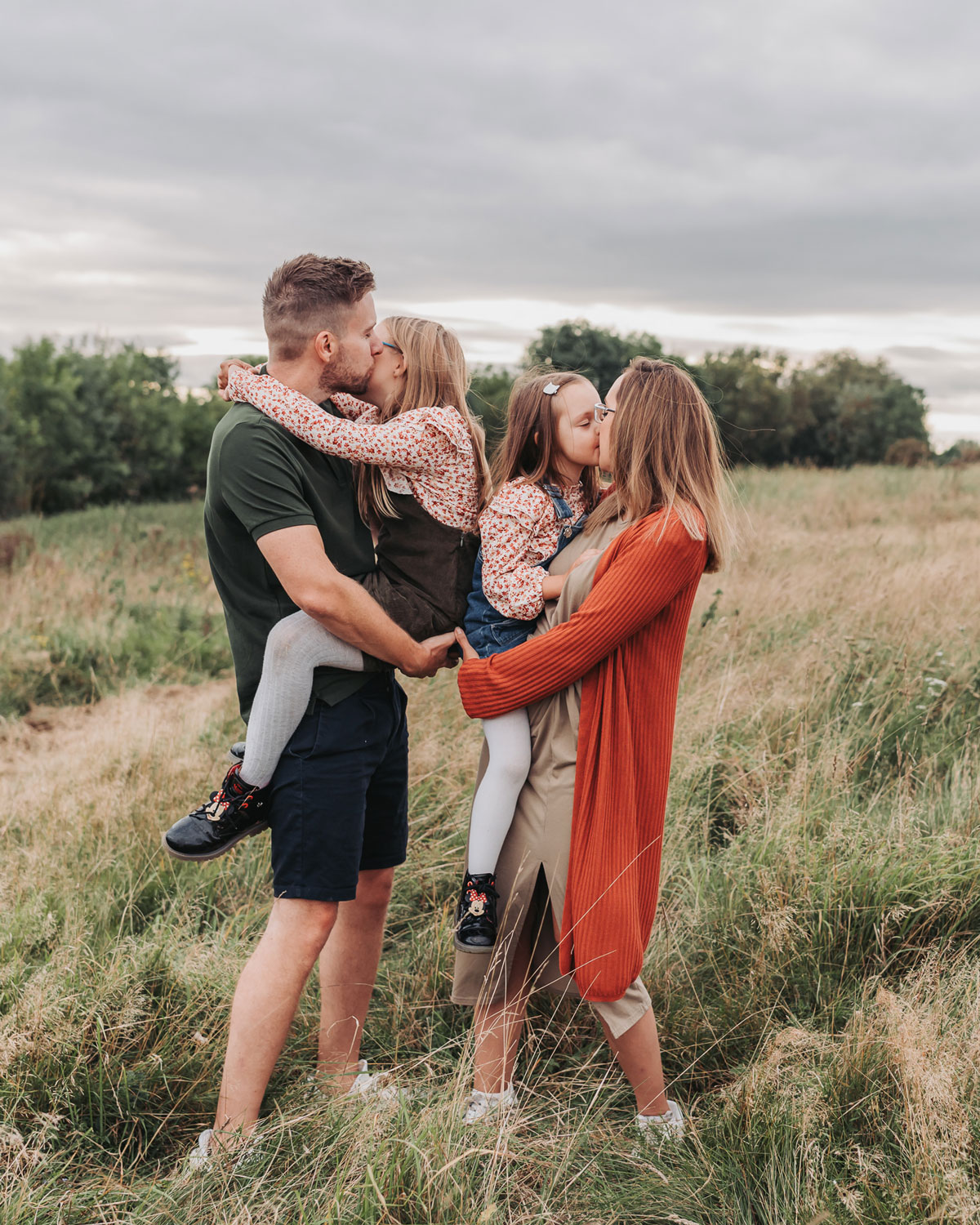 Parents holding children and kissing them in a meadow at a family photoshoot by The Corbett Creative Photography
