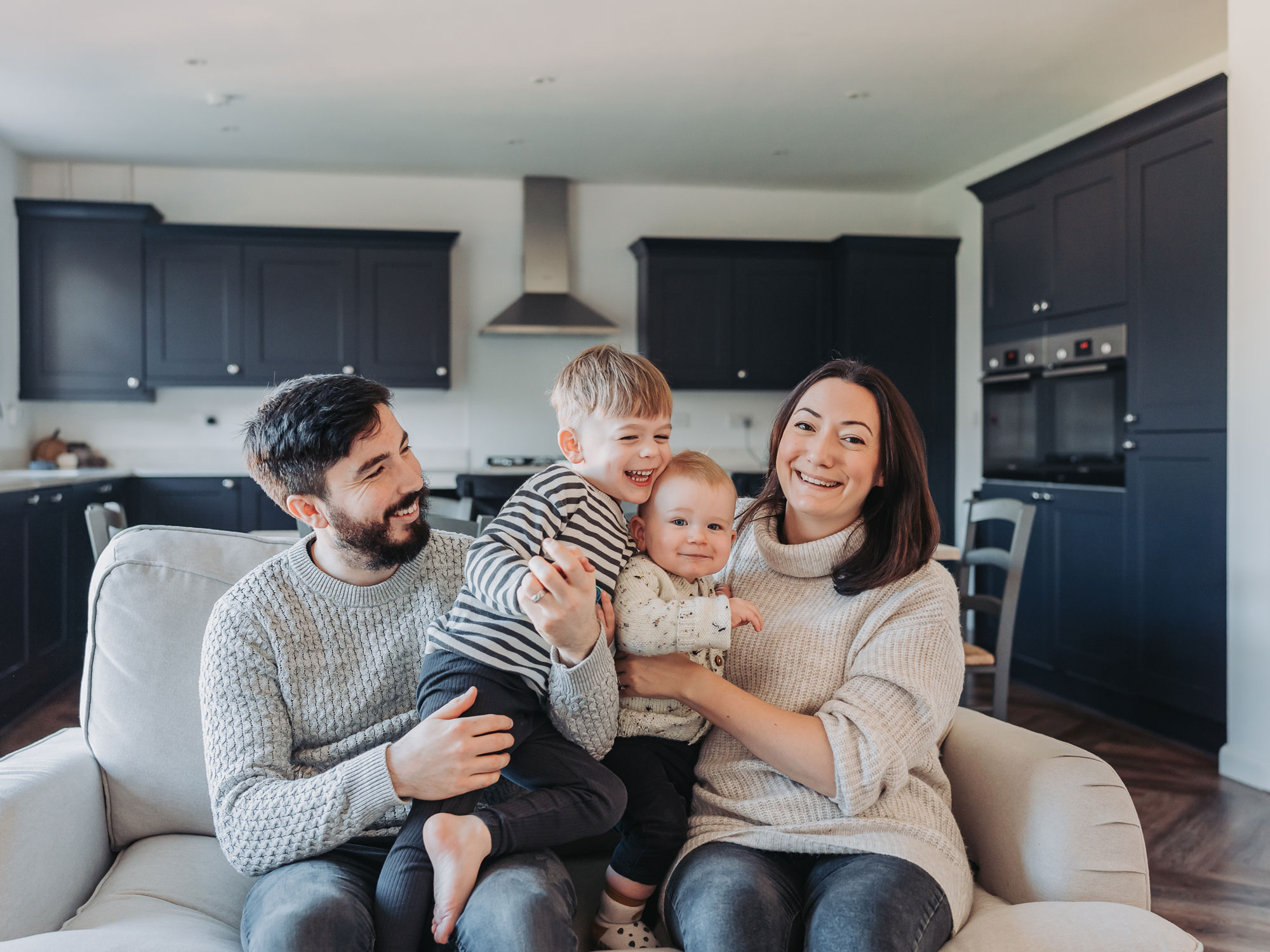 Family cuddled together on the sofa in a kitchen during an at home family photoshoot in Warwickshire