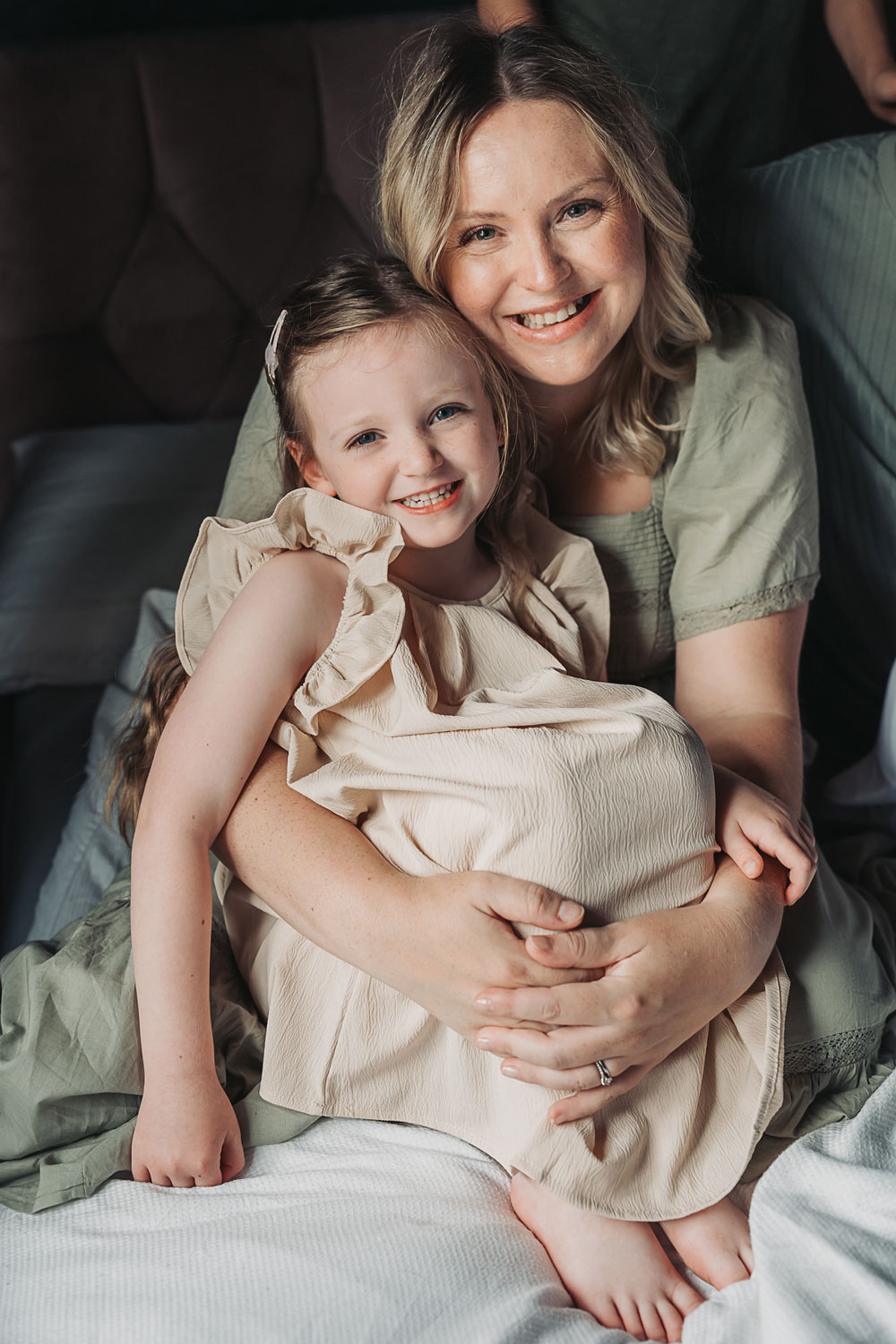 Mum smiling at camera whilst cuddling daughter during an at home newborn photoshoot