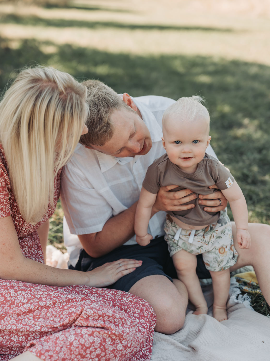 Blonde baby wearing shorts smiling at the camera during an outdoor summer family photoshoot