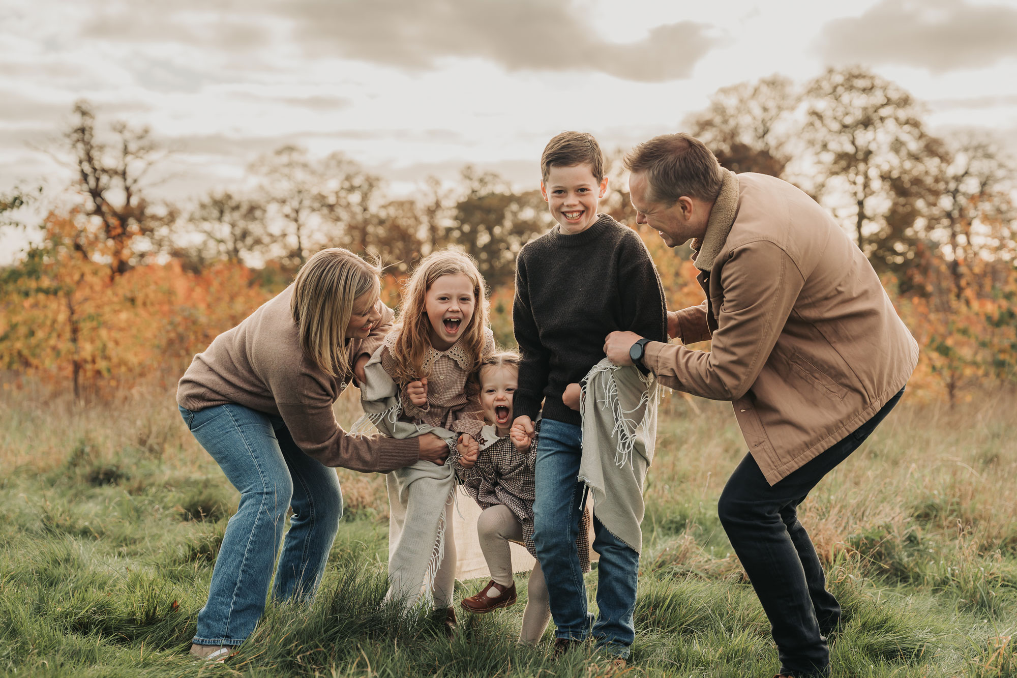 Parents wrapping up three children in a blanket during an autumn family photoshoot in Warwickshire by The Corbett Creative Photography