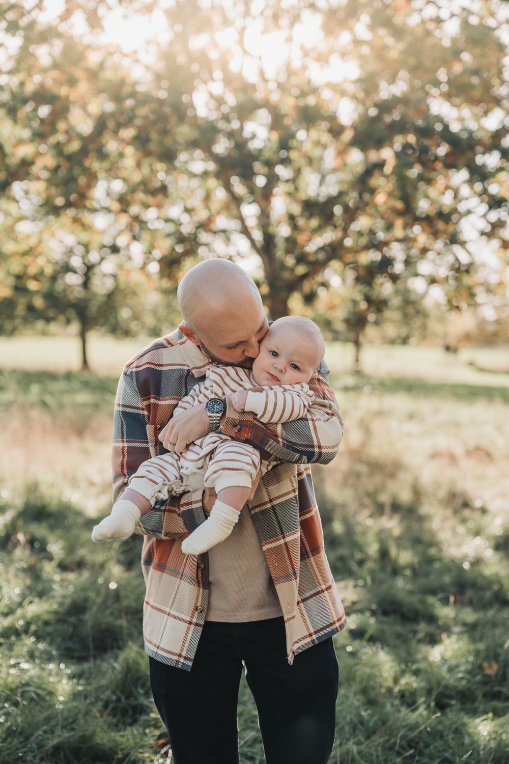 Dad cuddling baby during an outdoor autumn family photoshoot in Stratford Upon Avon