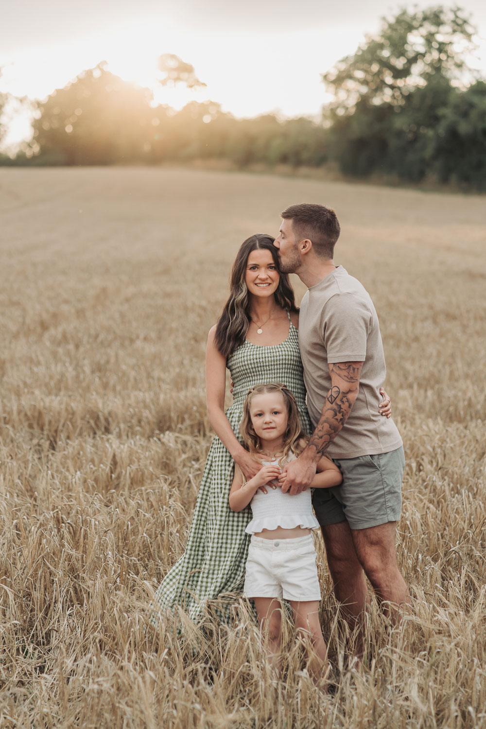 Crop field golden hour family photoshoot with dad kissing mum's head