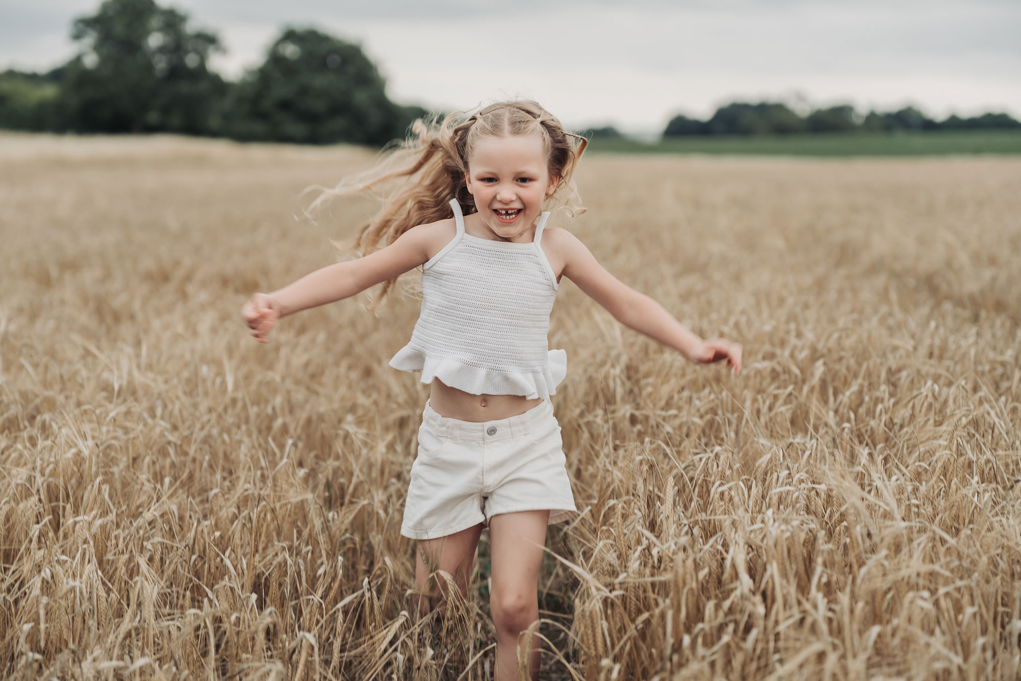 Crop field golden hour family photoshoot with little girl running through crop field