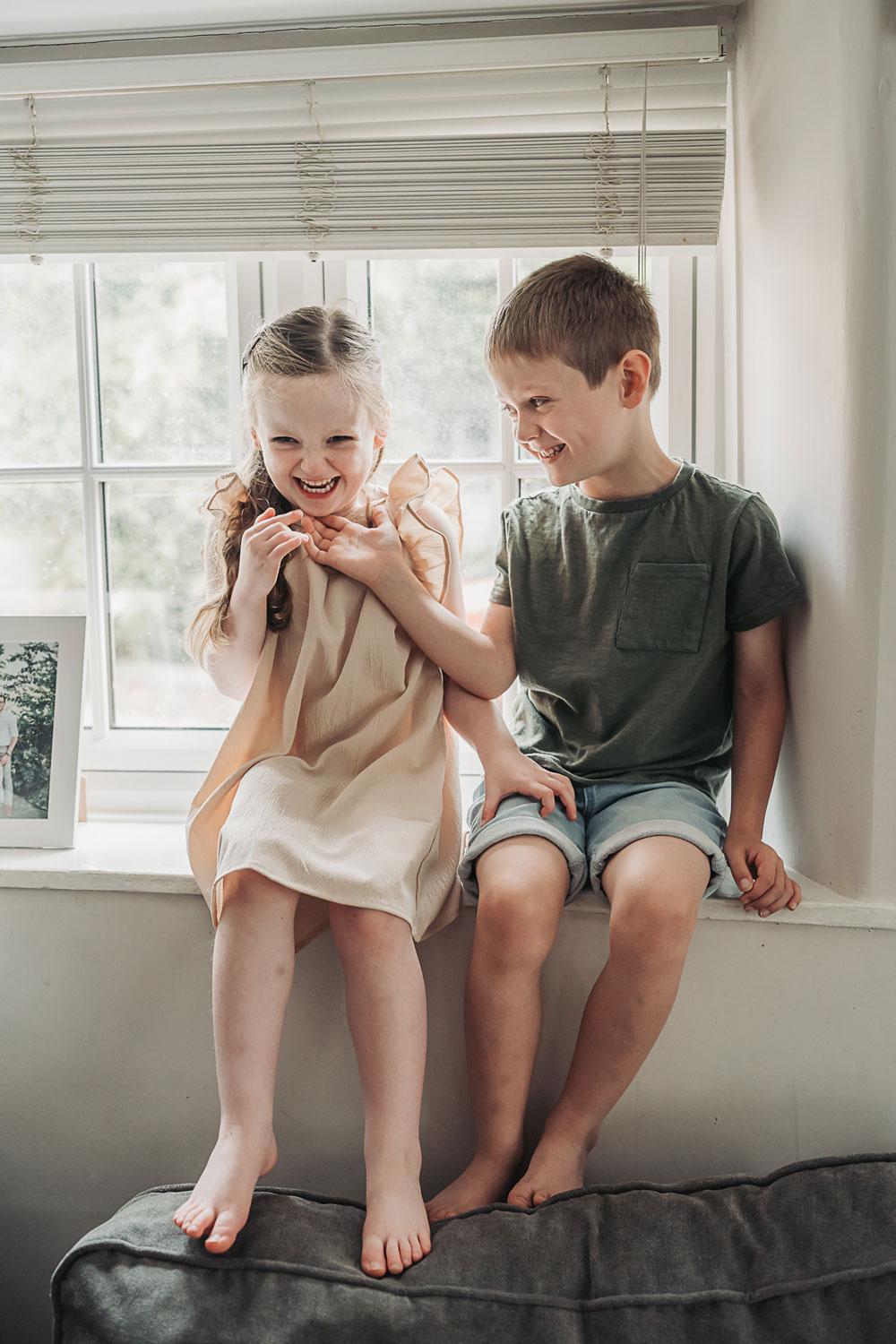 children sat on windowsill tickling eachother during an at home newborn photoshoot in northamptonshire