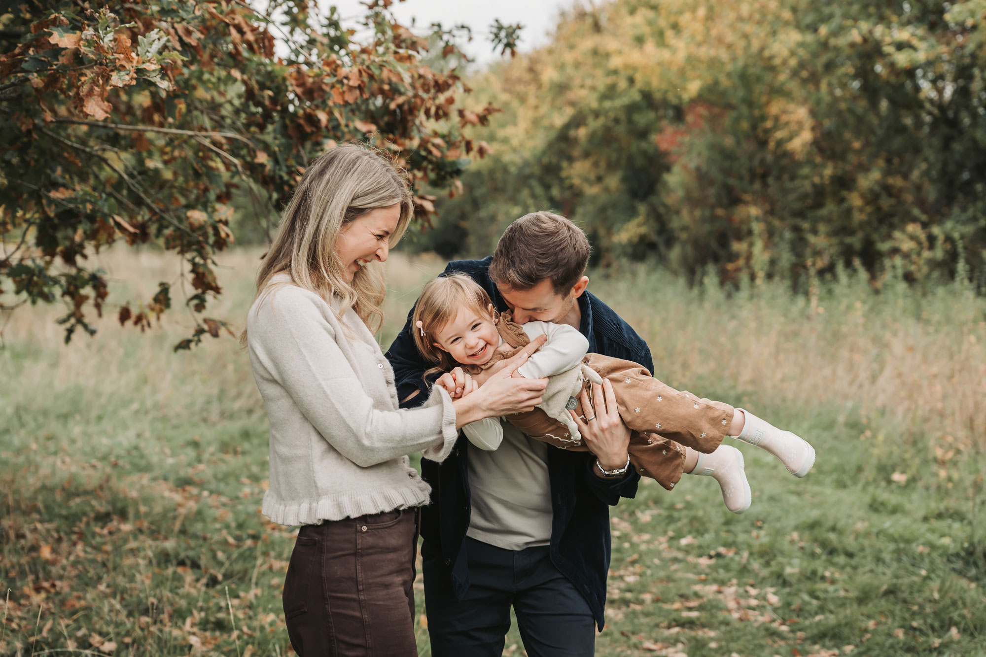 Stratford-Upon-Avon outdoor autumn family photoshoot with parents cuddling up toddler girl and smiling