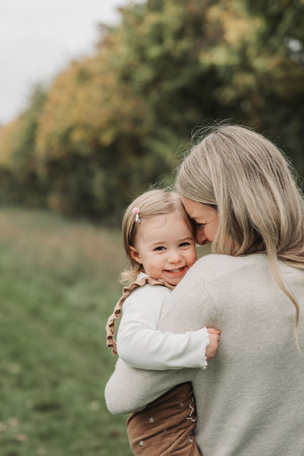 Stratford-Upon-Avon outdoor autumn family photoshoot with Mum cuddling little toddler girl who is smiling at camera