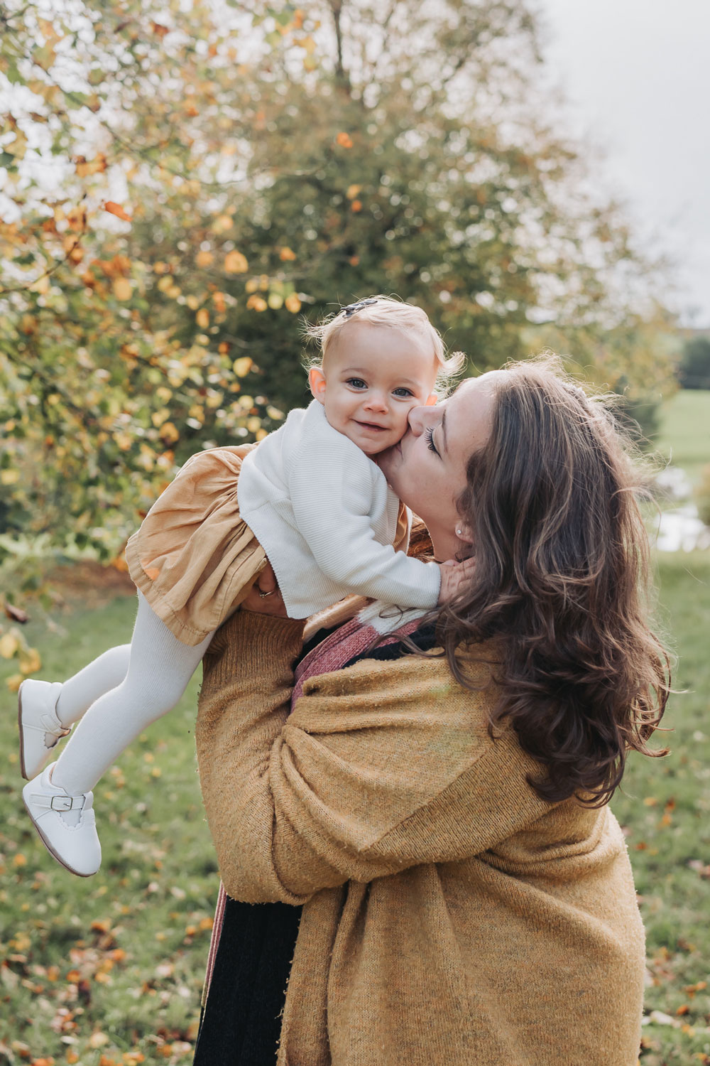 toddler girl being kissed and hugged by mum during a Warwickshire autumn photoshoot