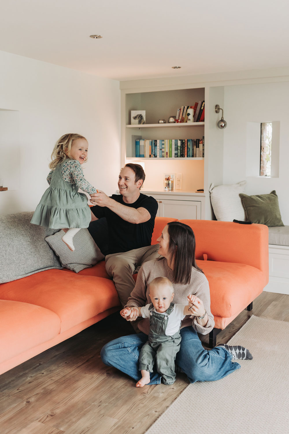 In home family photoshoot with Warwickshire family on orange sofa with little girl jumping