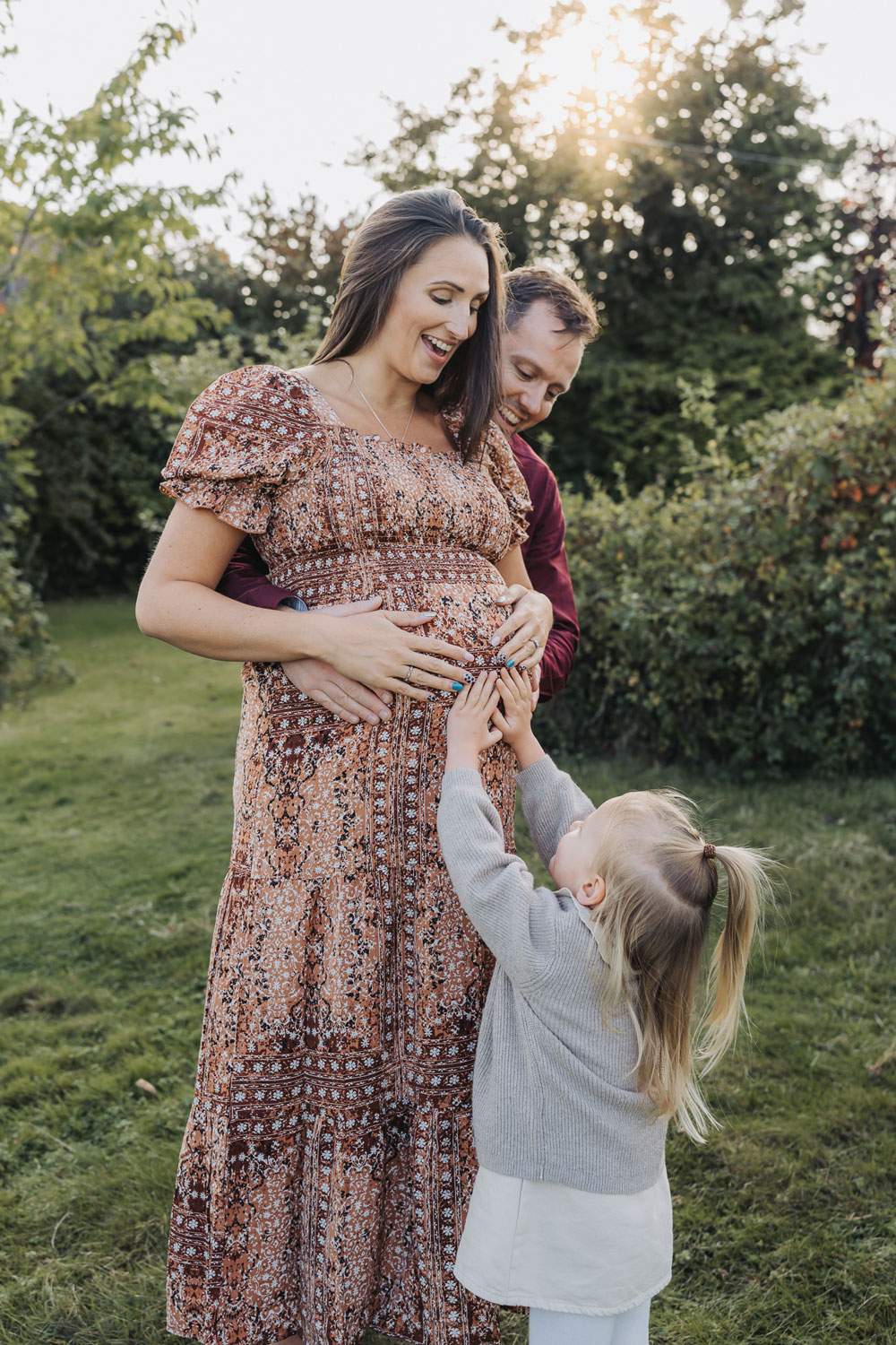 Outdoor golden hour maternity photoshoot with toddler girl touching mum's bump