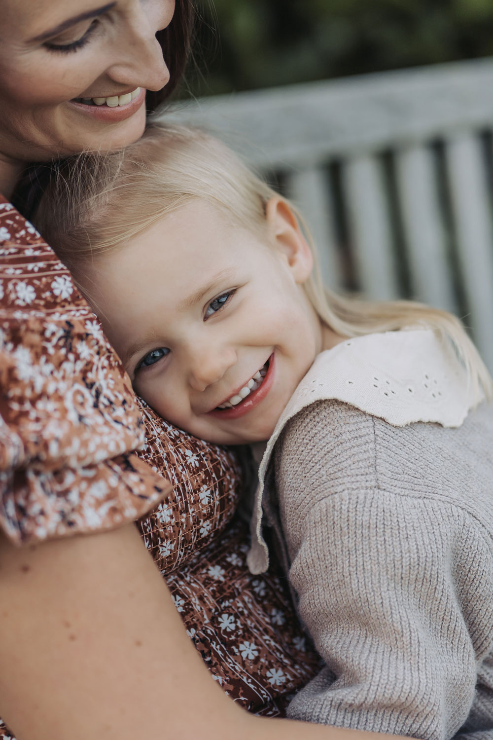 Outdoor golden hour maternity photoshoot with little girl cuddling mum and smiling at camera
