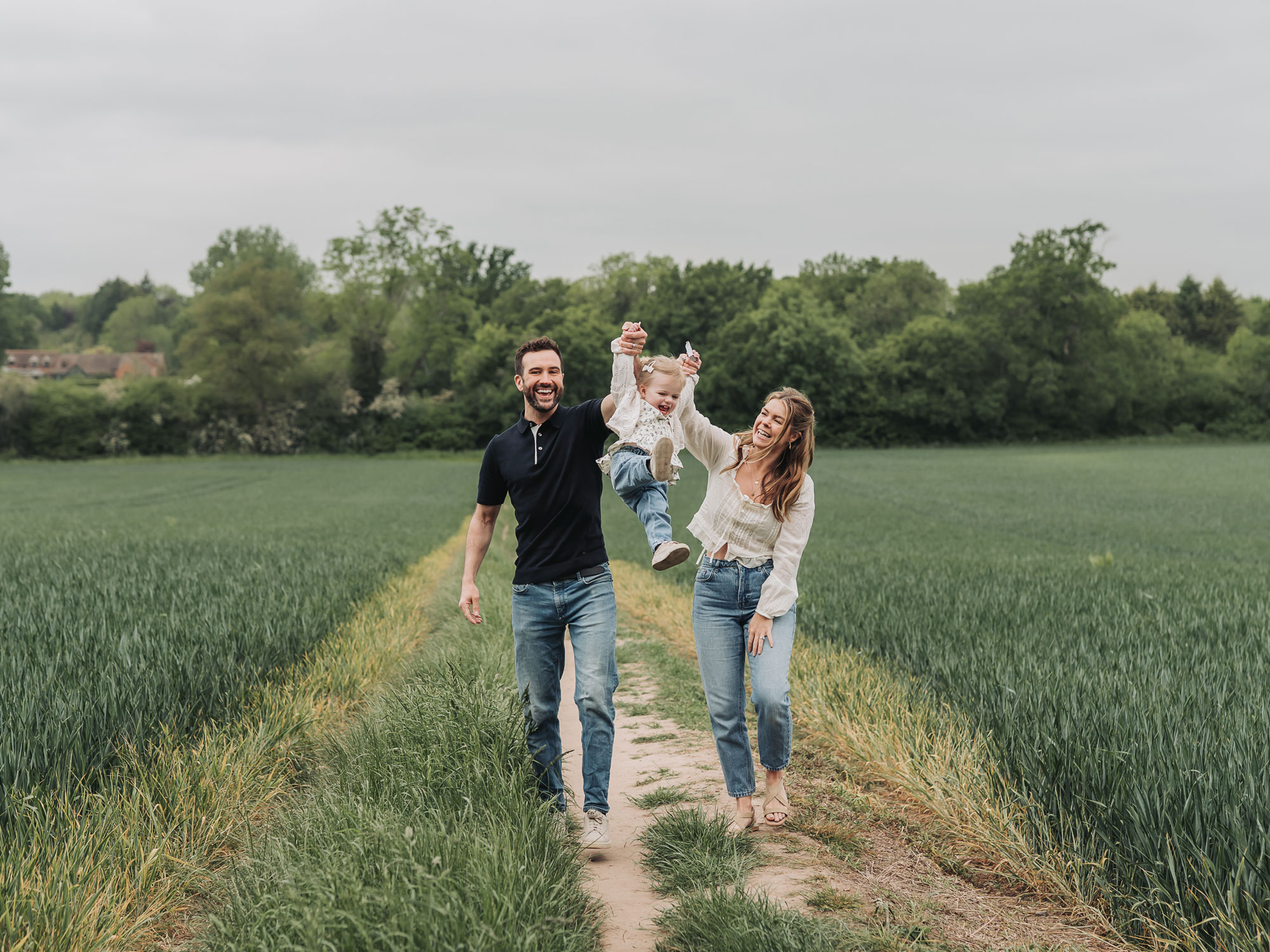 Warwickshire crop field photoshoot with family walking and swinging toddler daughter