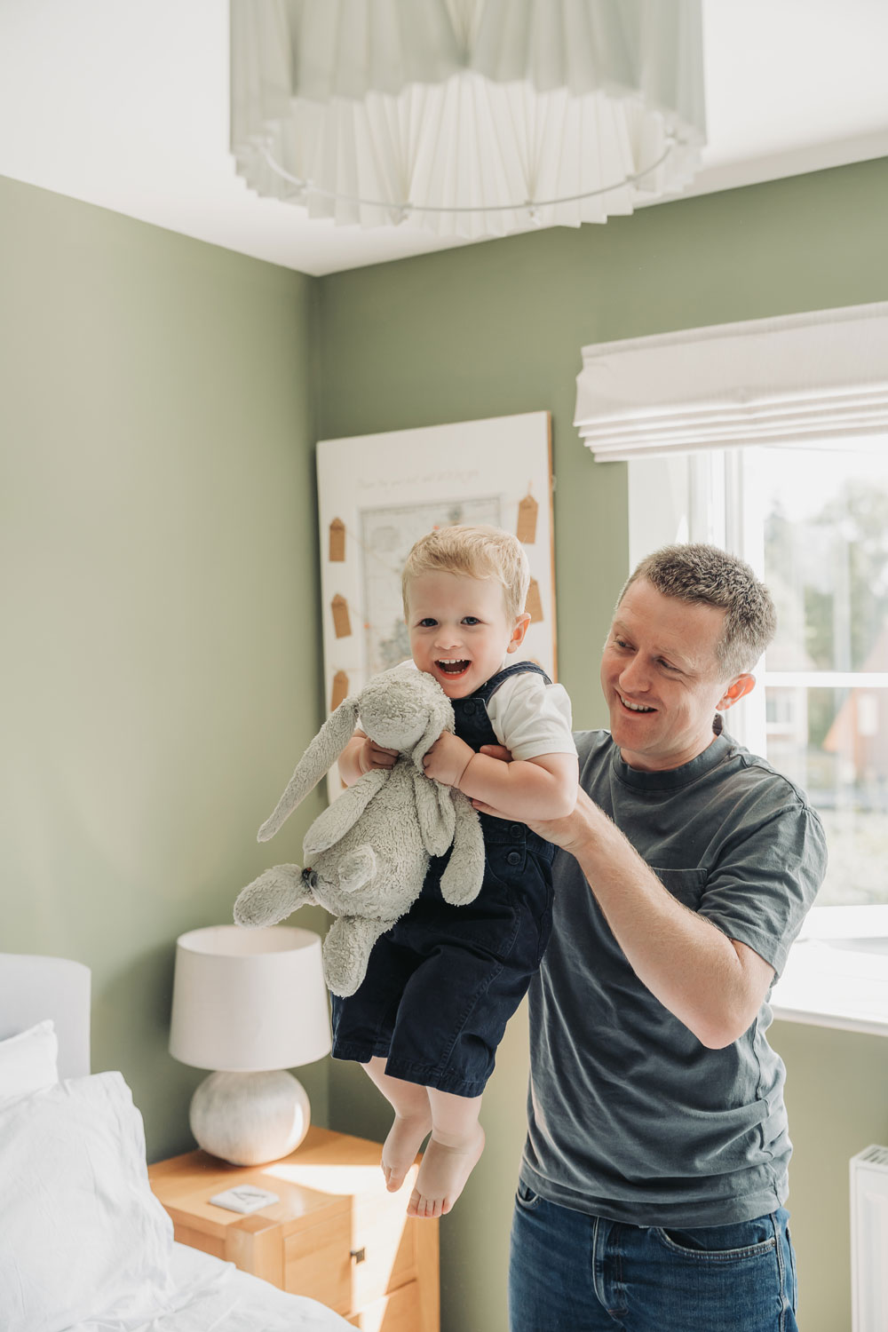 In home newborn photoshoot with dad picking up toddler and swinging him