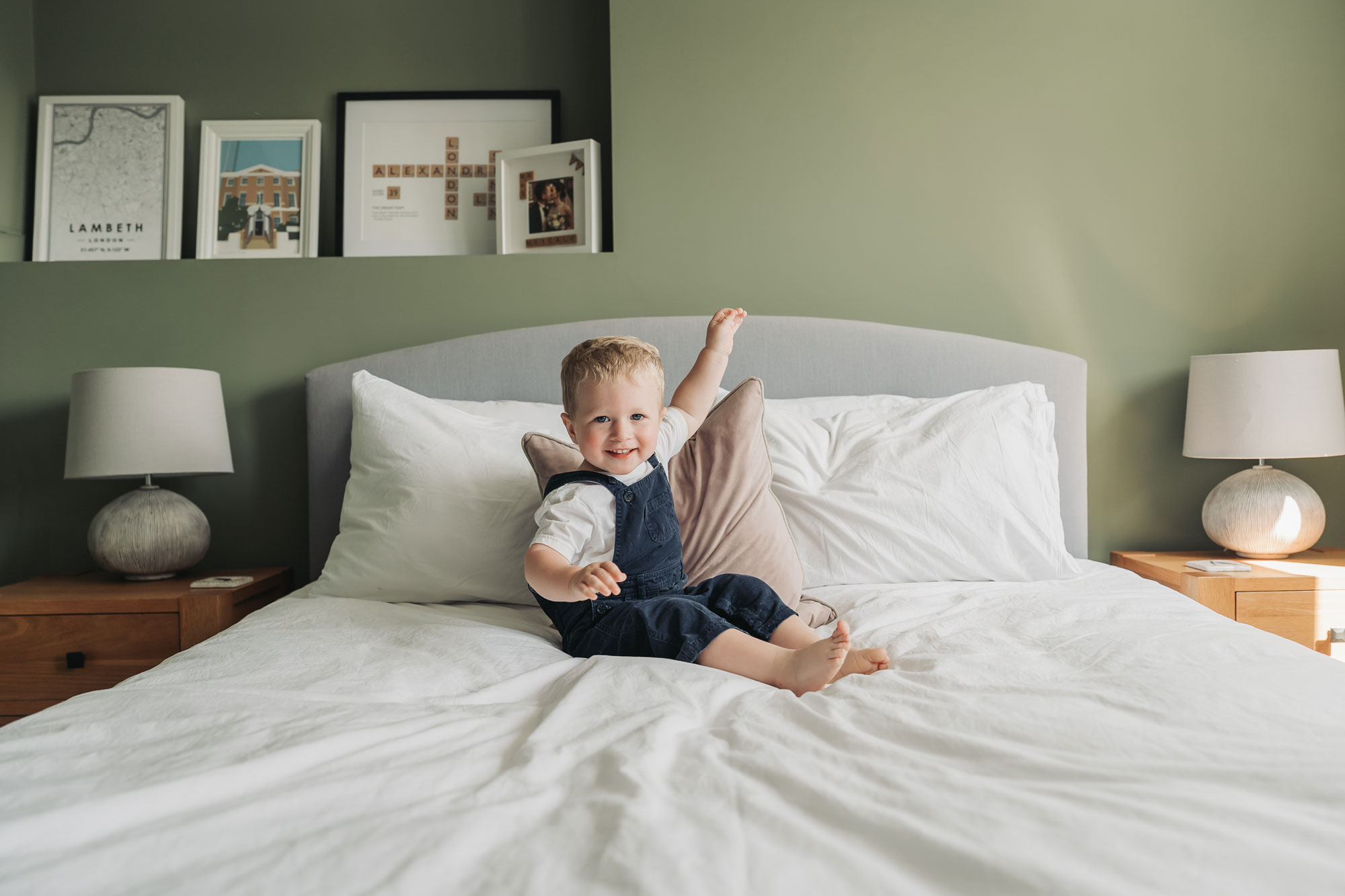 In home newborn photoshoot with toddler boy sat on bed smiling