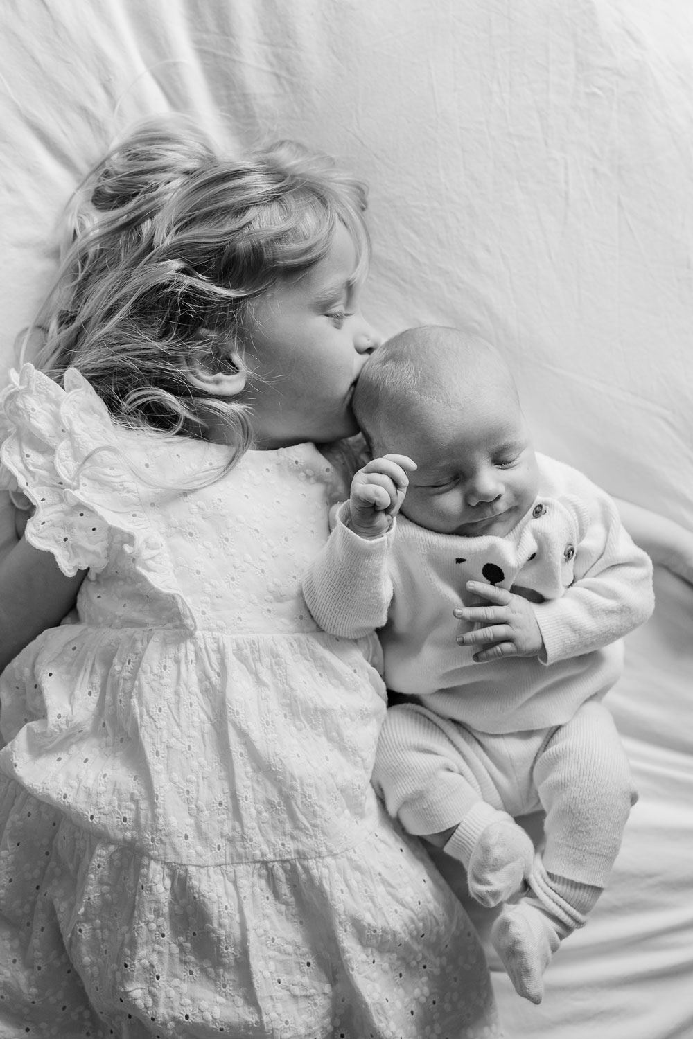black and white of little girl in white dress kissing asleep baby
