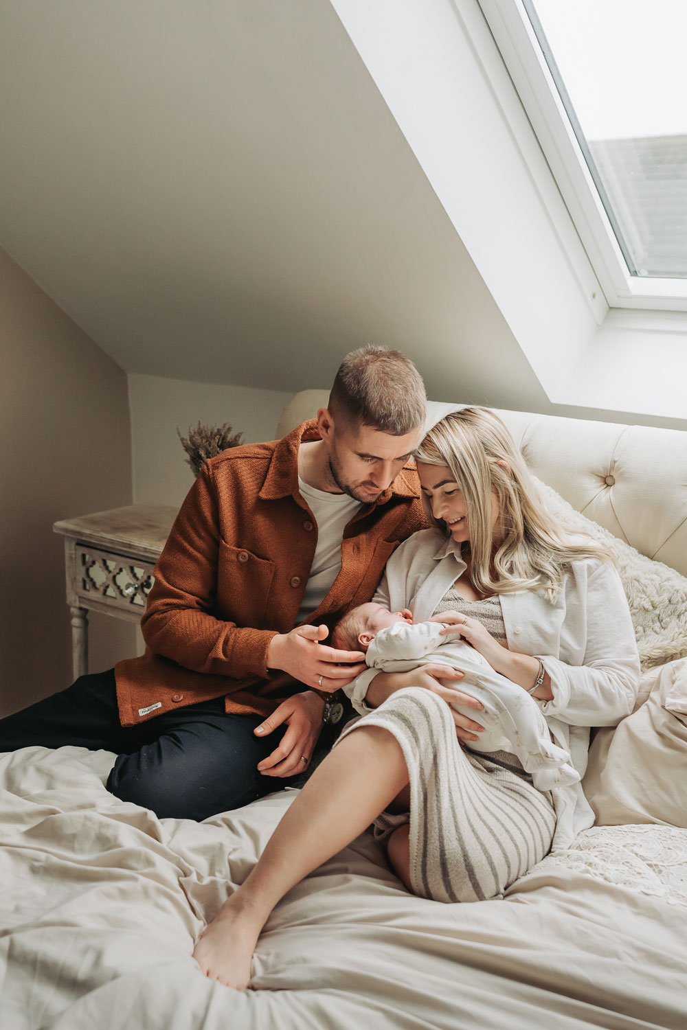 mum and dad cuddled on bed whilst holding newborn baby