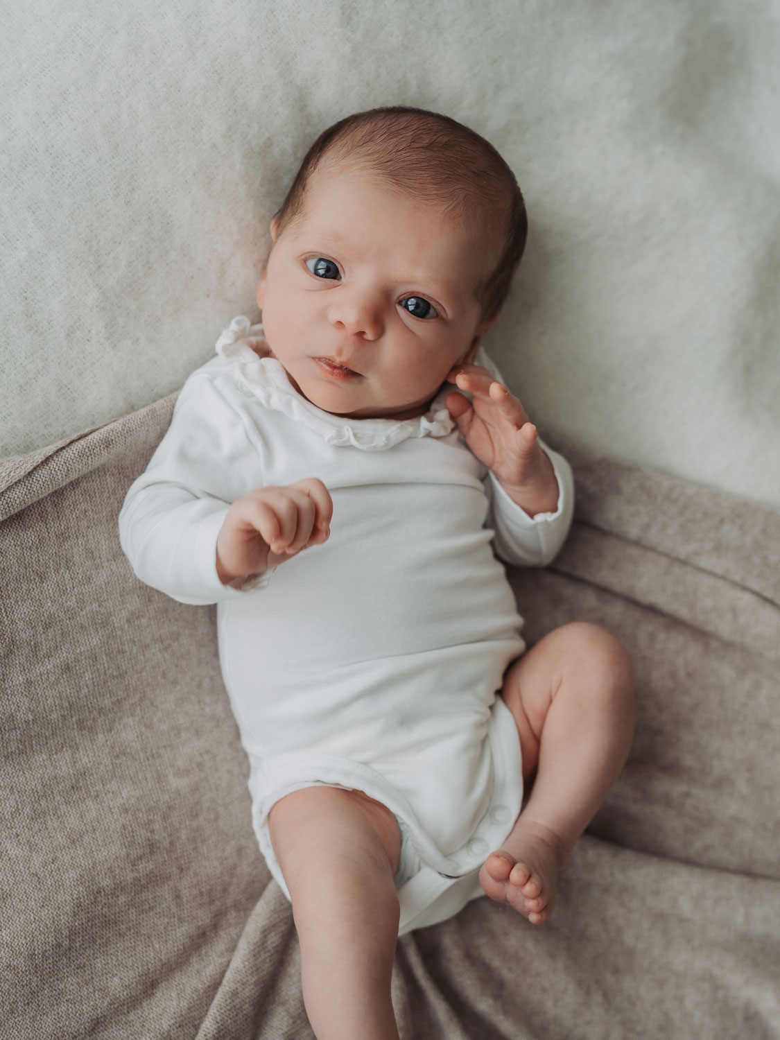 newborn baby wearing white vest awake looking at camera