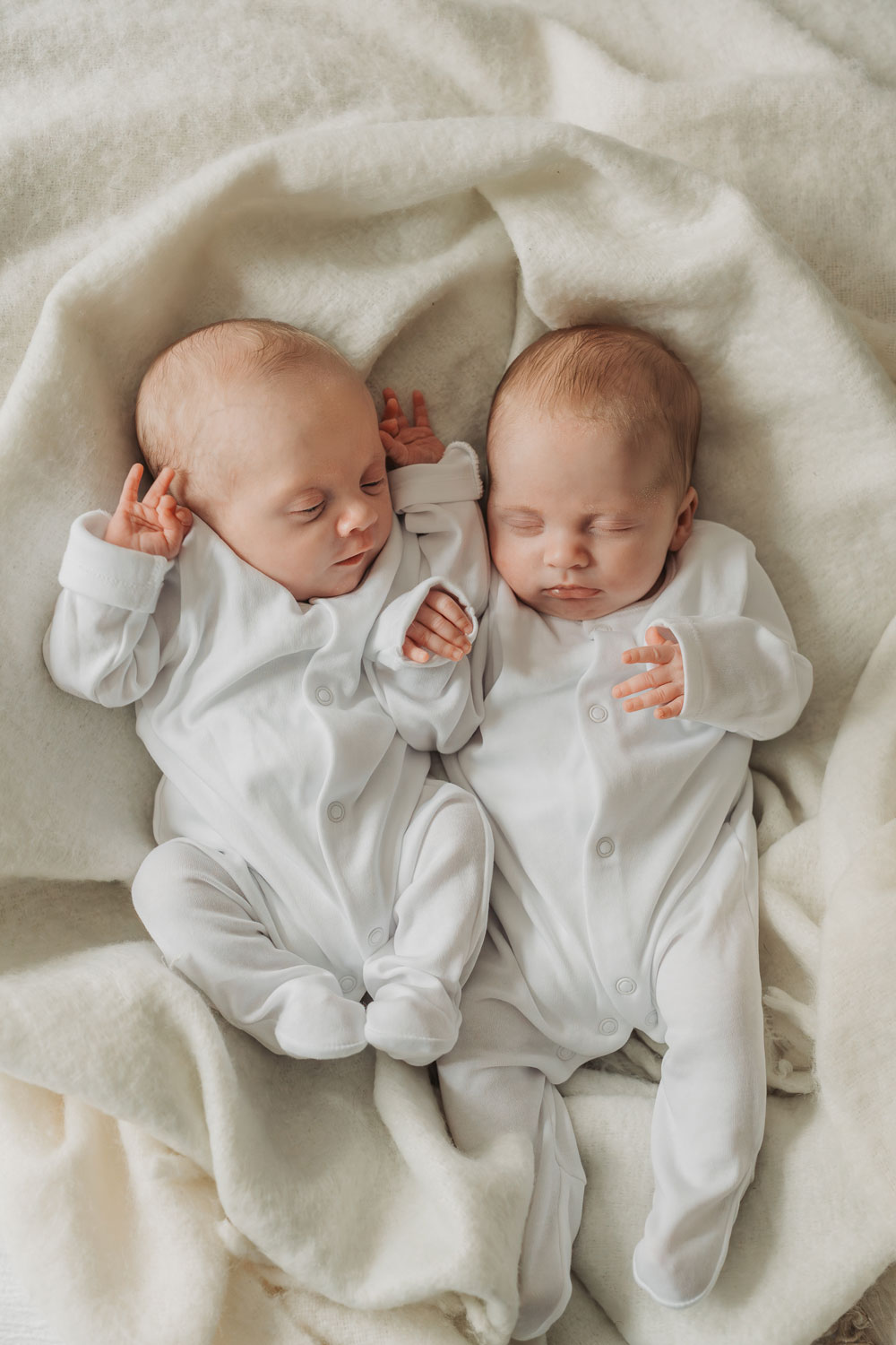 twins cuddled together asleep wearing white babygrows