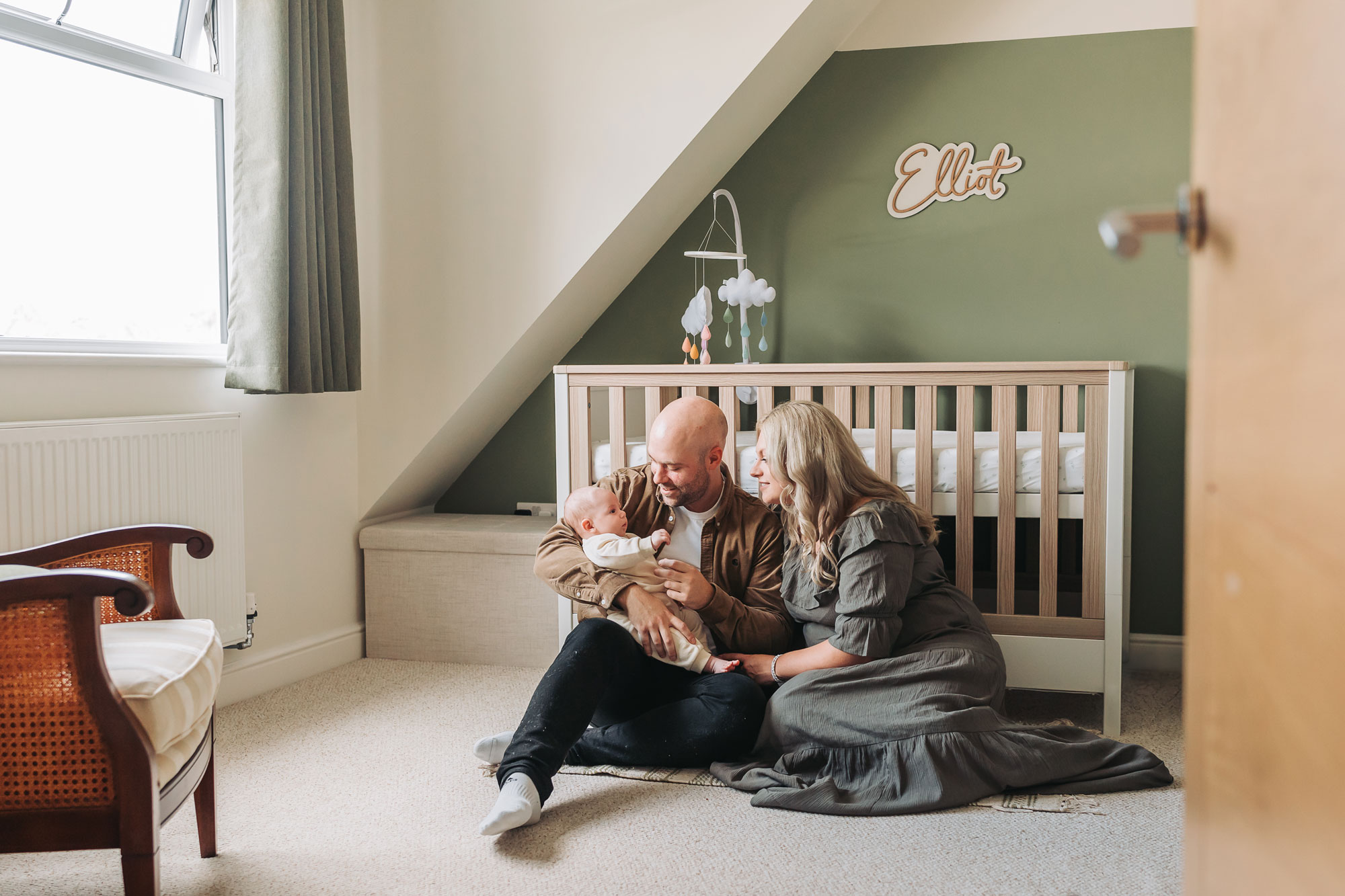 baby sat on nursery floor holding baby under a sign that says Elliot