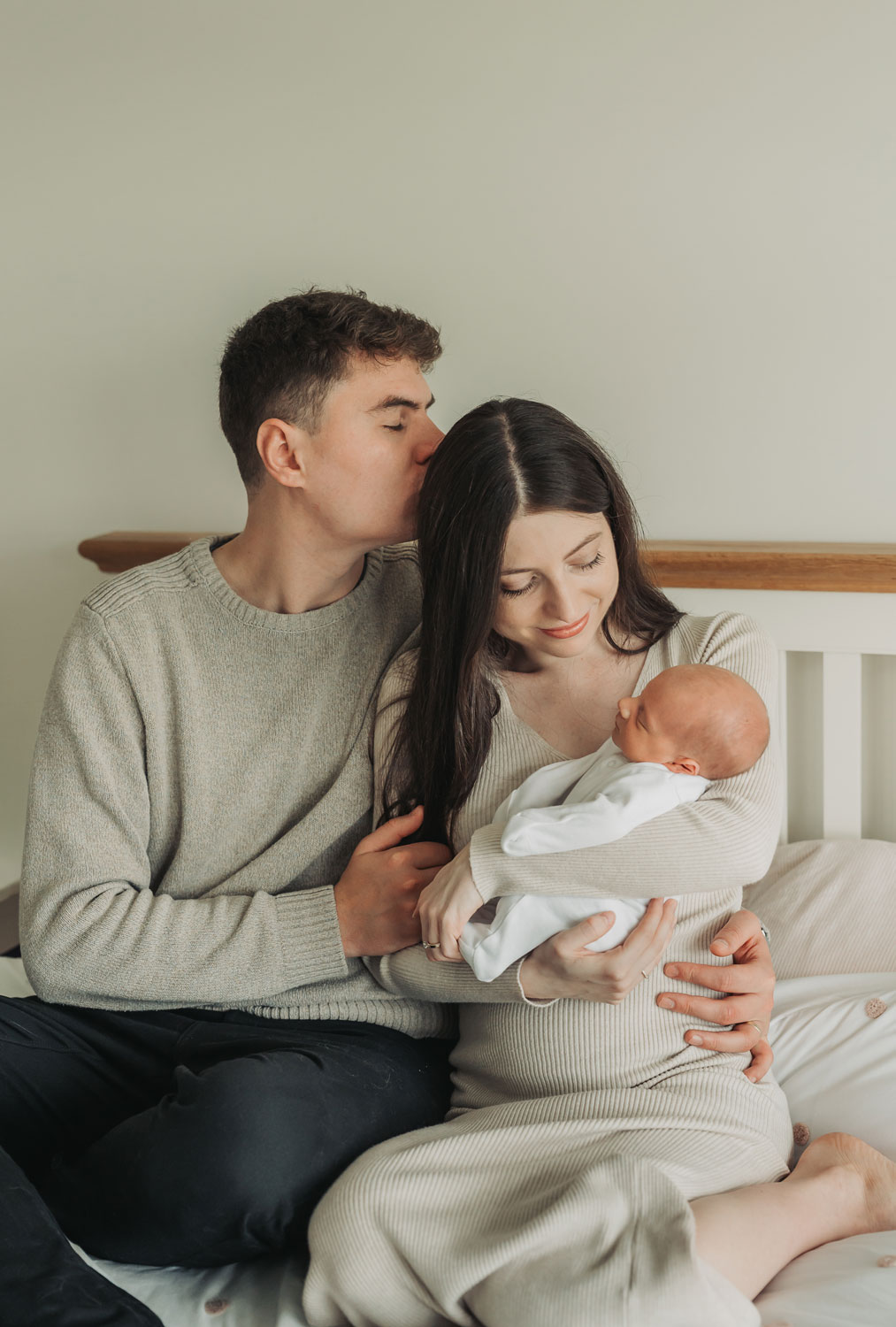 dad kissing mum on hear whilst she holds baby