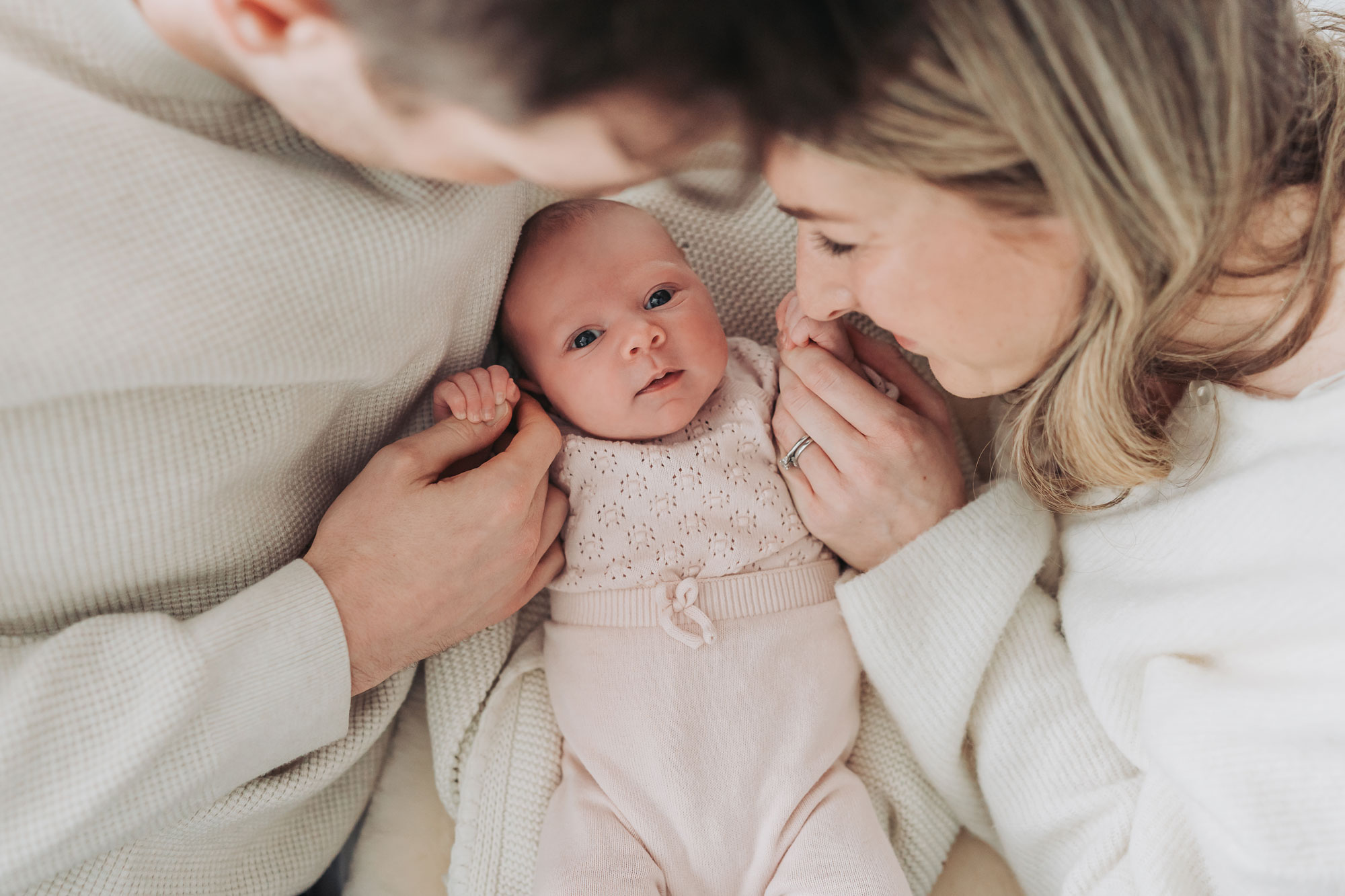 Leamington family lying on bed looking down at baby whilst she looks at camera