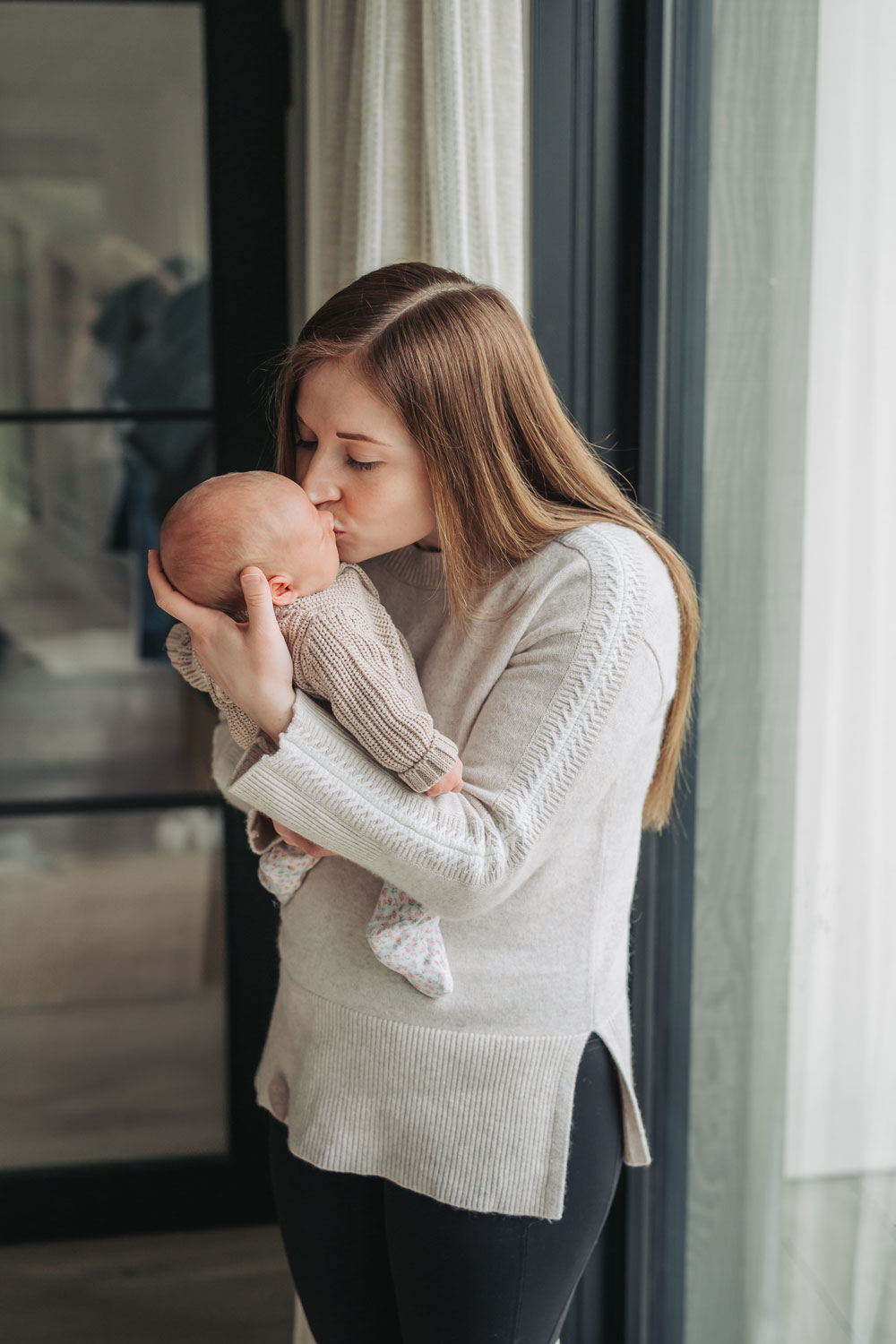 Mum in beige jumper stood kissing newborn baby in Stratford Upon Avon