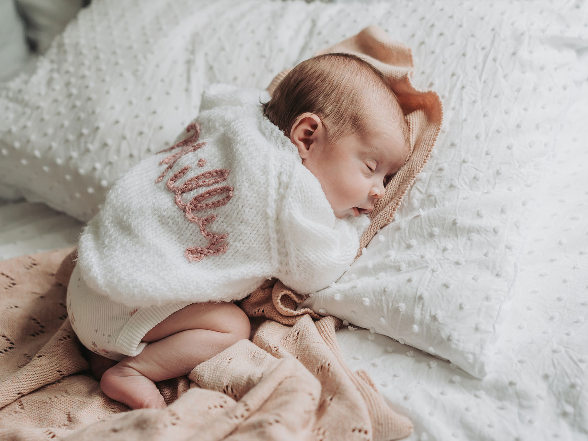 baby wearing knitted cardigan lying on pink blanket
