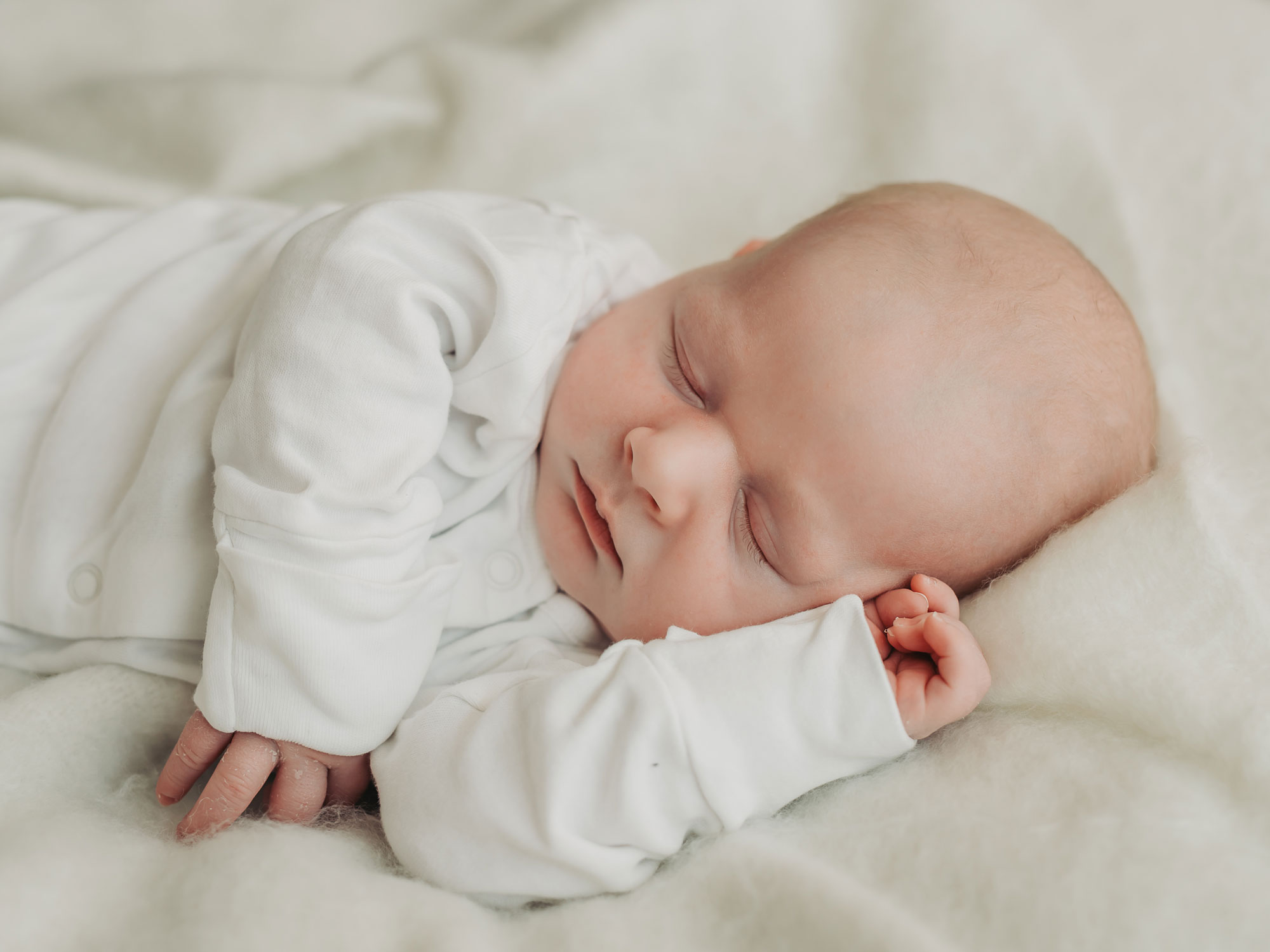 Side view of baby asleep wearing white babygrow