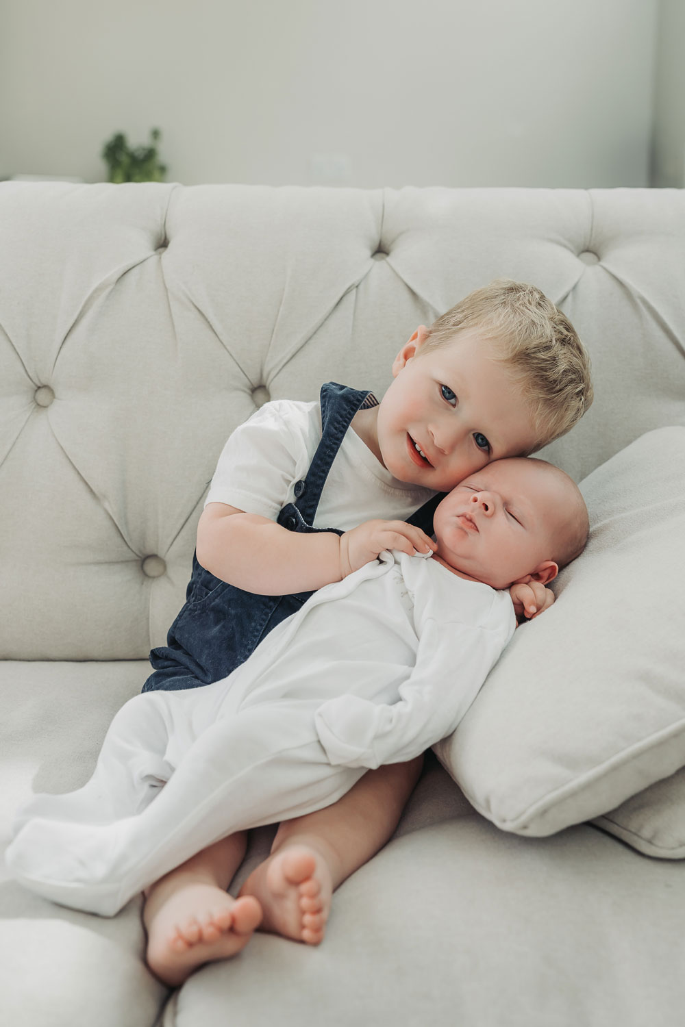 toddler sat on sofa cuddling newborn baby at kenilworth photoshoot