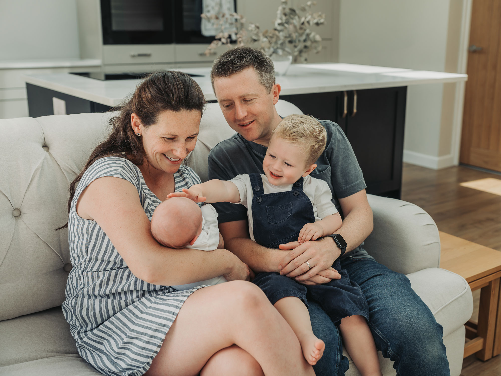 Kenilworth family sat on sofa with toddler touching newborn baby