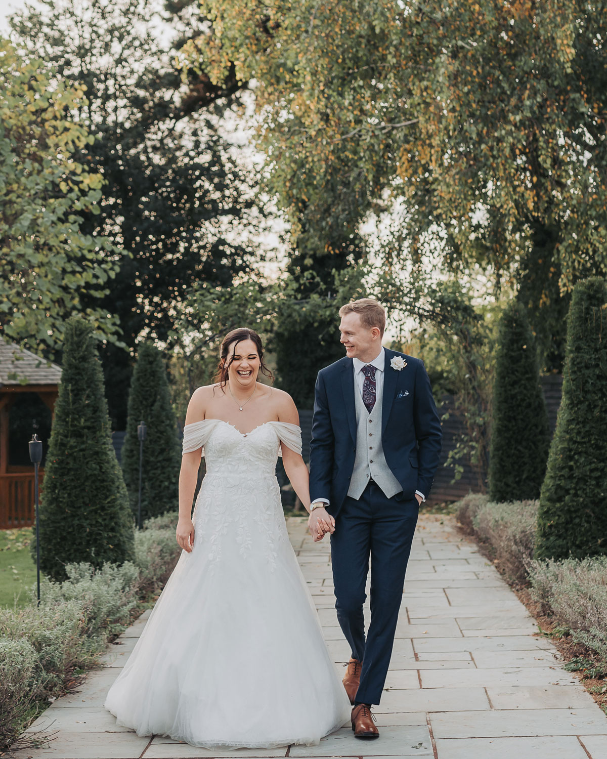 Couple portrait with bride laughing walking along pathway of Ashton Lodge wedding venue Warwickshire