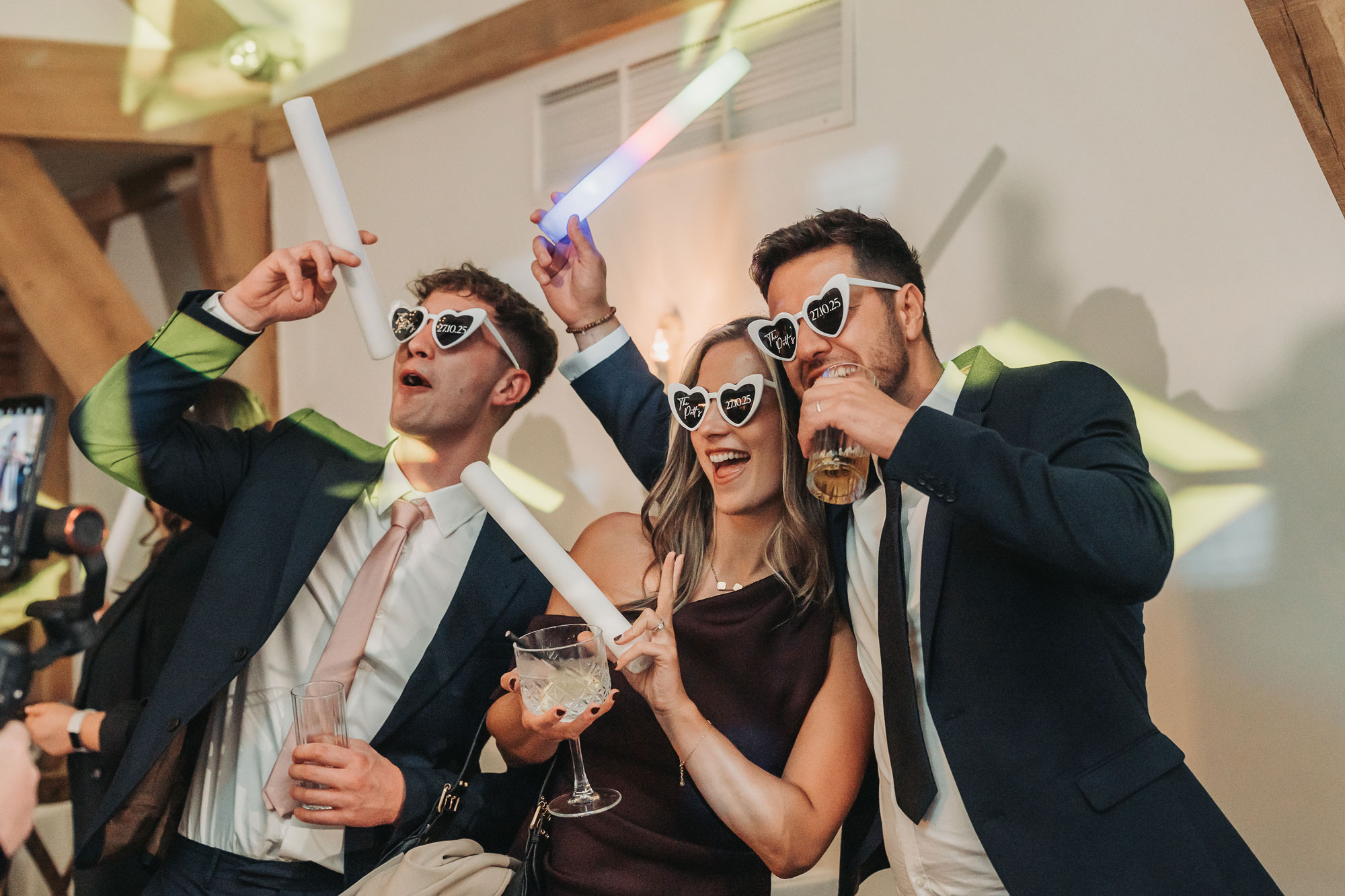 Mythe barn wedding guests with glow sticks and glasses on dancefloor looking happy