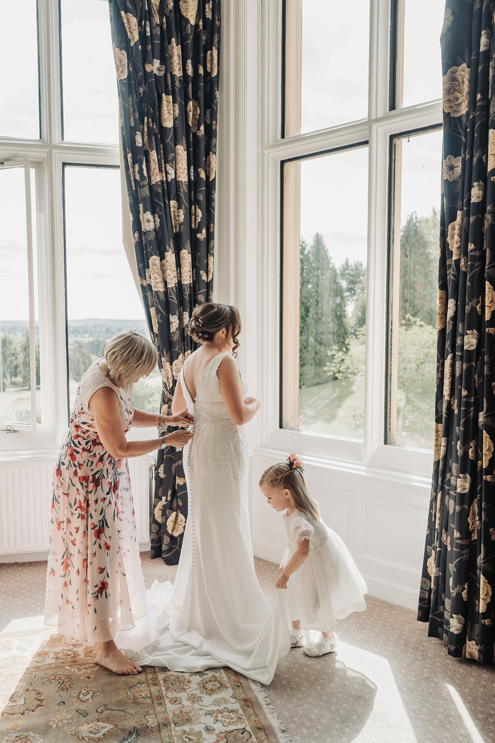 Bride getting into wedding dress at Welcombe Hotel in Stratford with mum and flower girl