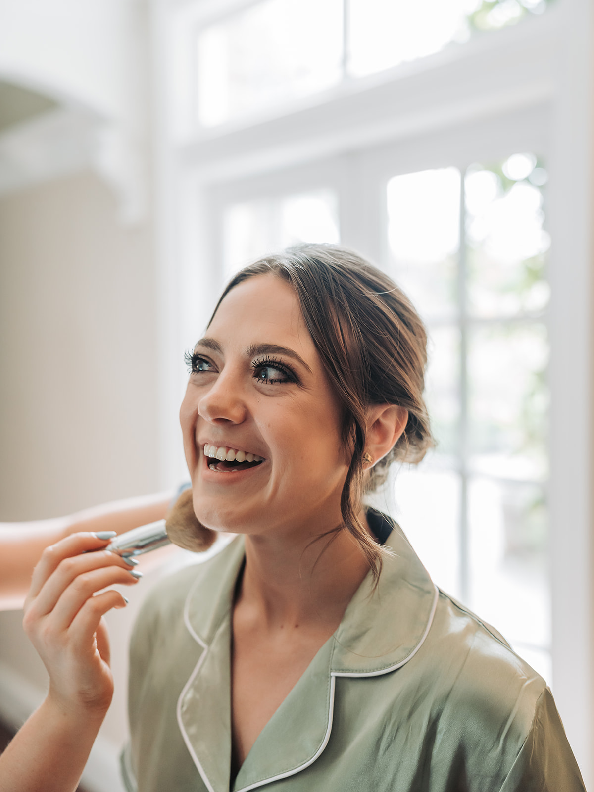 Close up of bridesmaid smiling wearing sage green pyjamas whilst having her make-up done