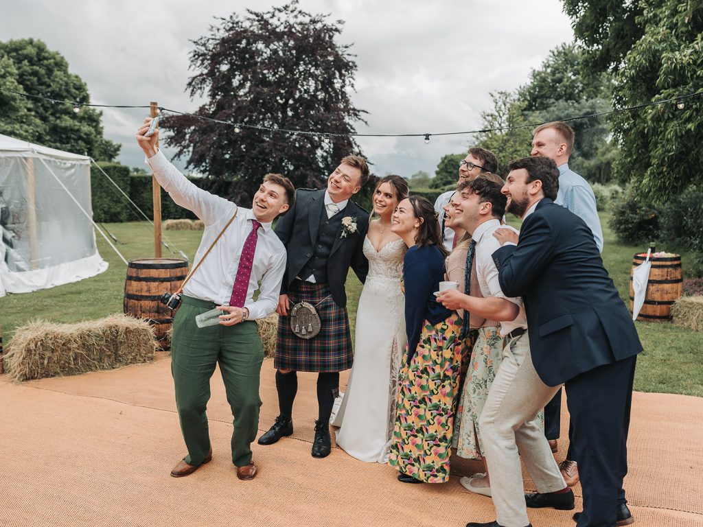 Bride, groom and wedding guests taking a group selfie at wedding
