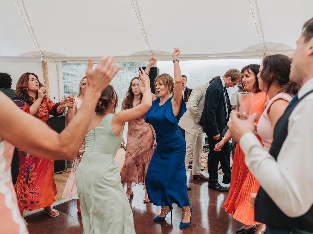 Wedding guest in blue dress dancing with arms up high