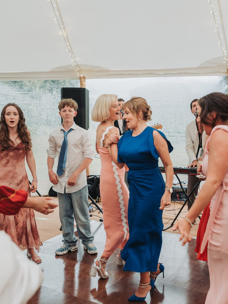 Wedding guests in dresses swinging arm in arm on dancefloor