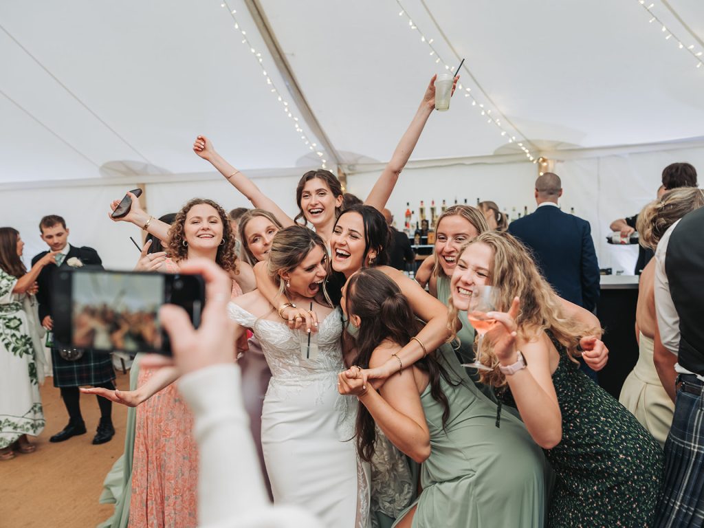 Bride with friends having fun whilst photo taken on phone