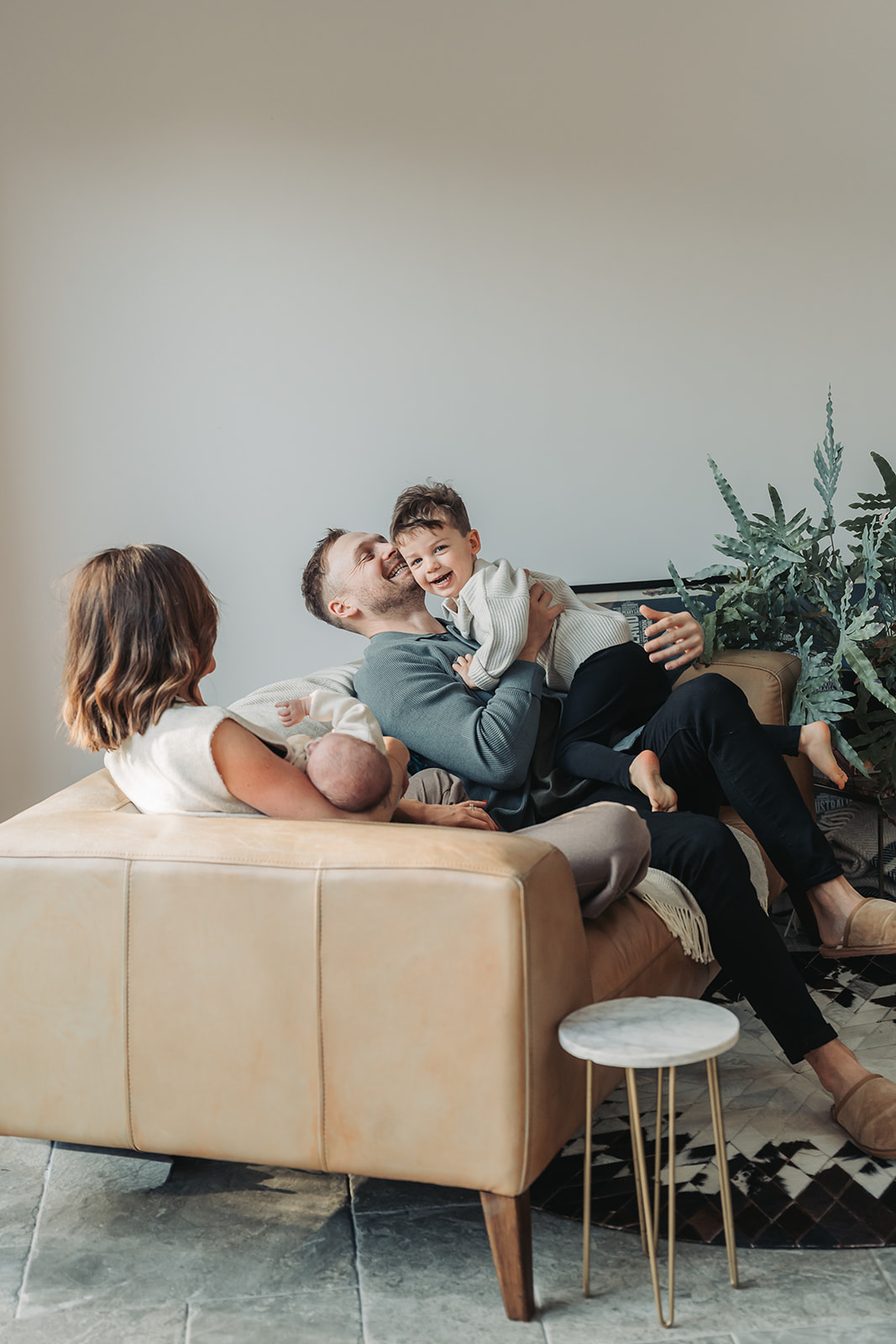 Dad and little boy cuddling and laughing on sofa during a newborn photoshoot at home in Kenilworth