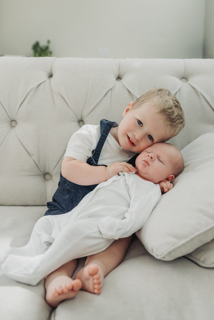 Toddler boy wearing dungaress cuddling baby on sofa at home
