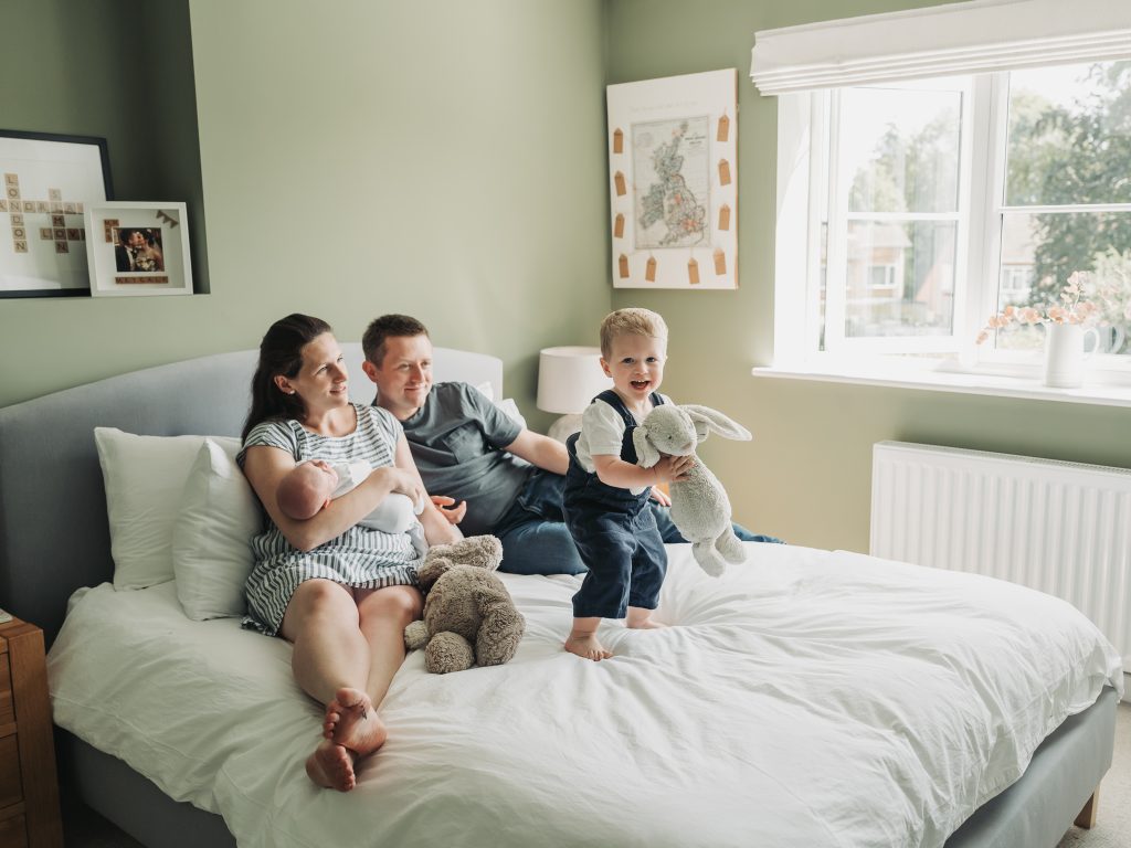 Toddler jumping on parents bed during an at home newborn photoshoot