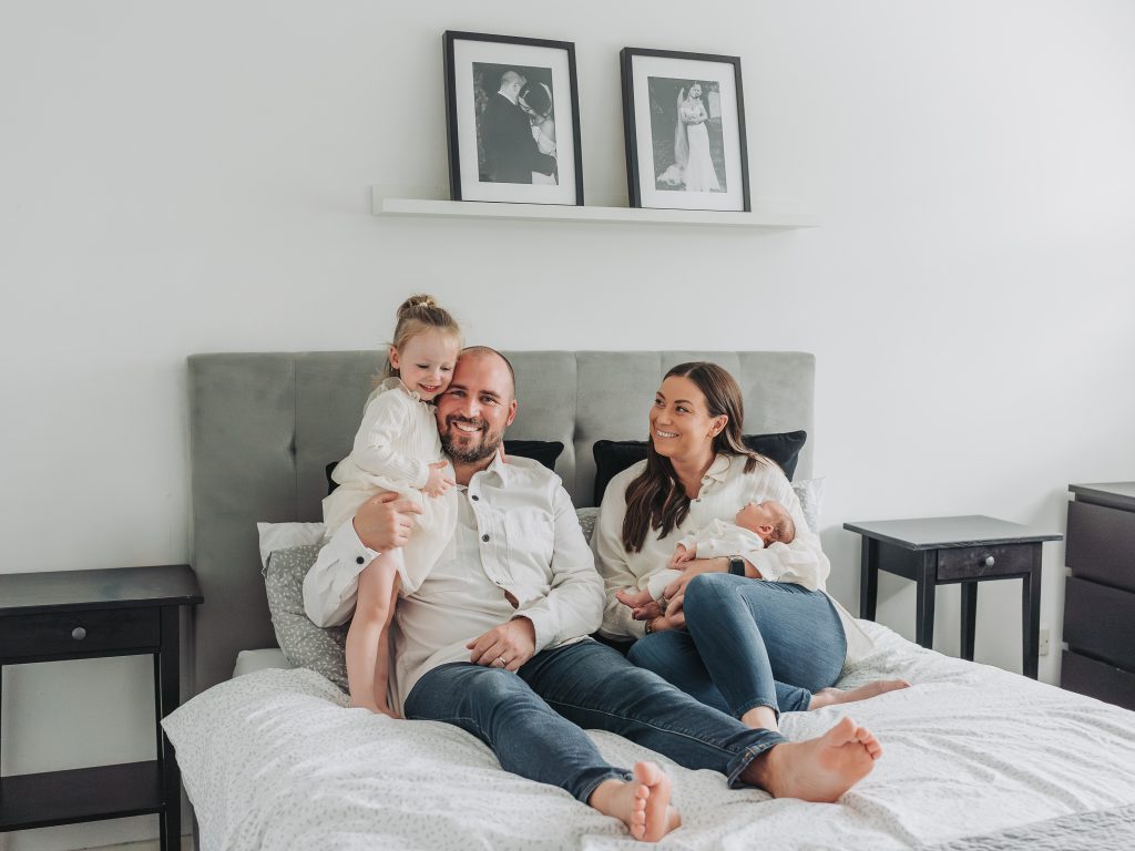 Mum and dad on bed with toddler and baby during a newborn photoshoot at home