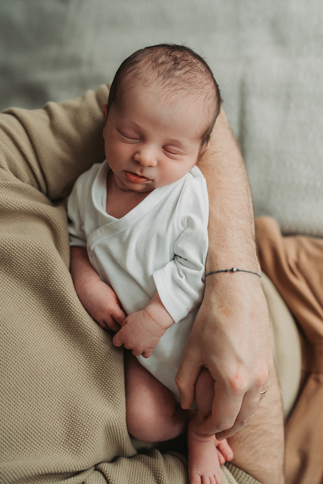 Close up of baby asleep in dad's arms wearing a white vest during a newborn in home photoshoot