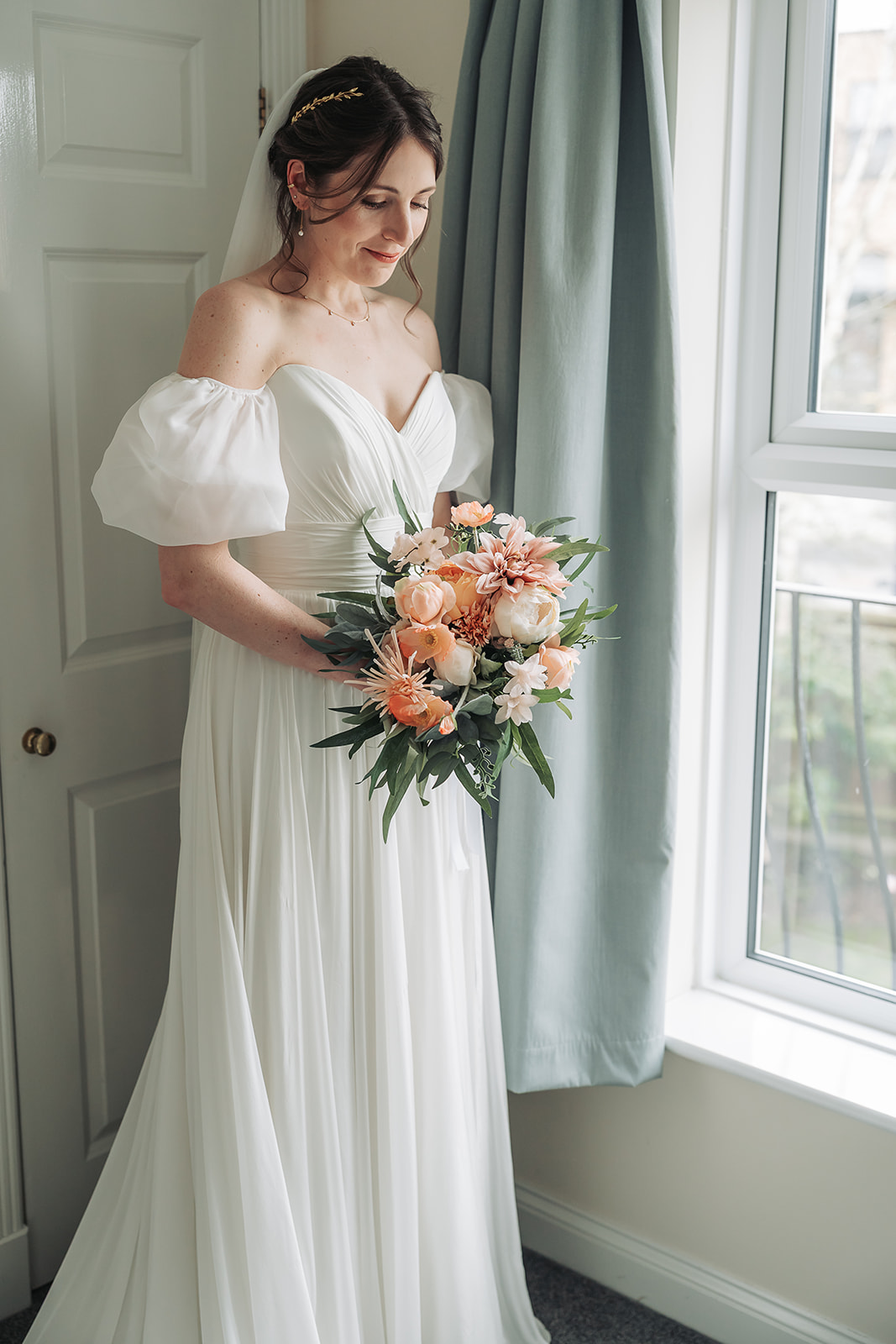 Bride wearing off the shoulder wedding dress gazing down at her peach bouquet